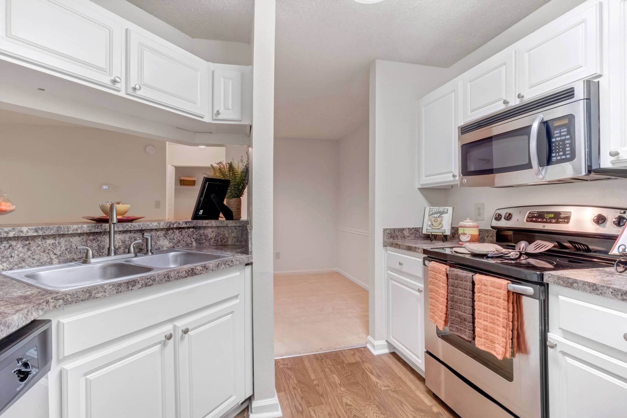 Modern kitchen with white cabinets, stainless steel appliances, and brown countertops with peach towels on oven.
