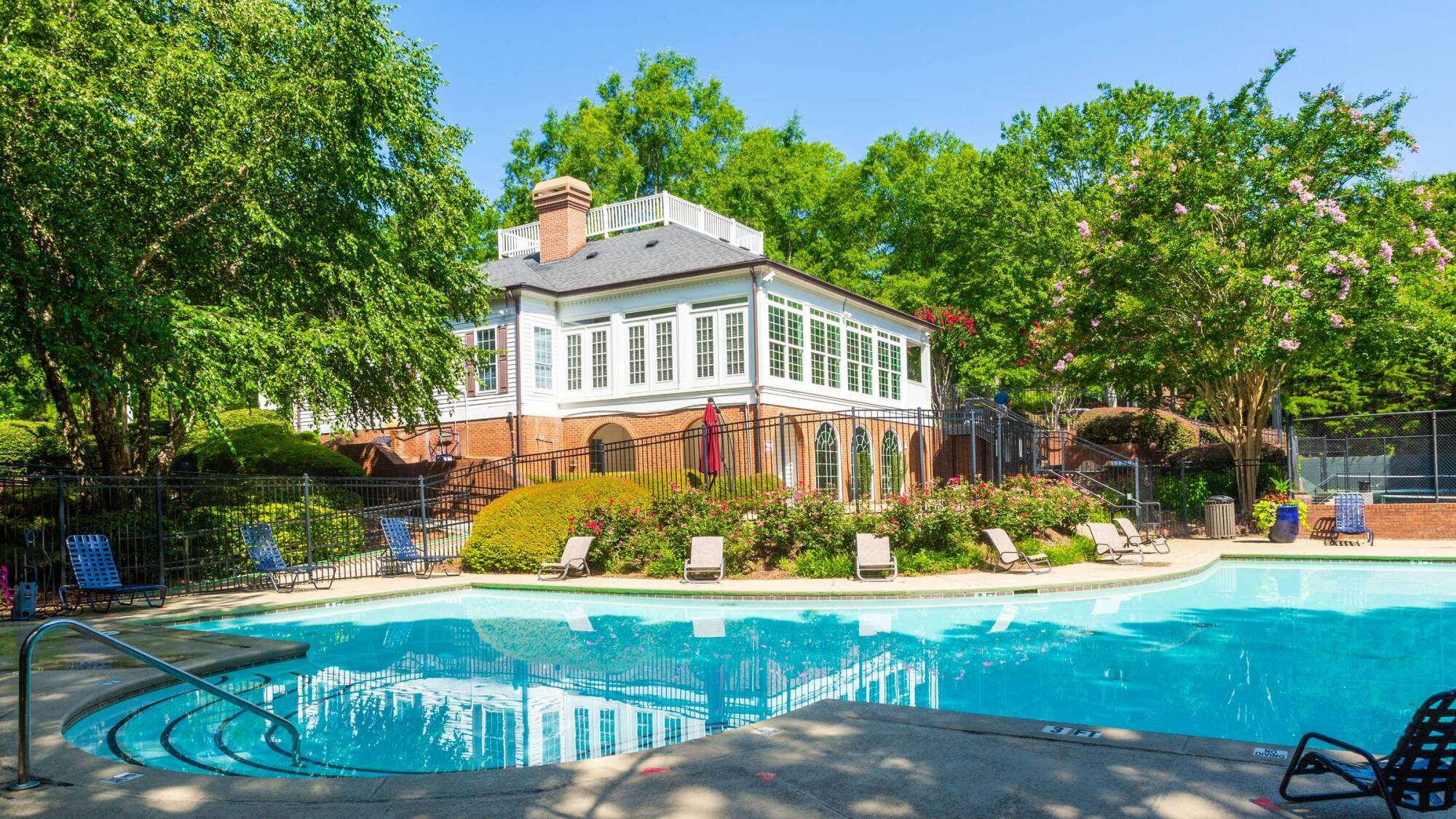Two-story apartment building with brick and beige siding, surrounded by trees, shrubs, and a grassy lawn.