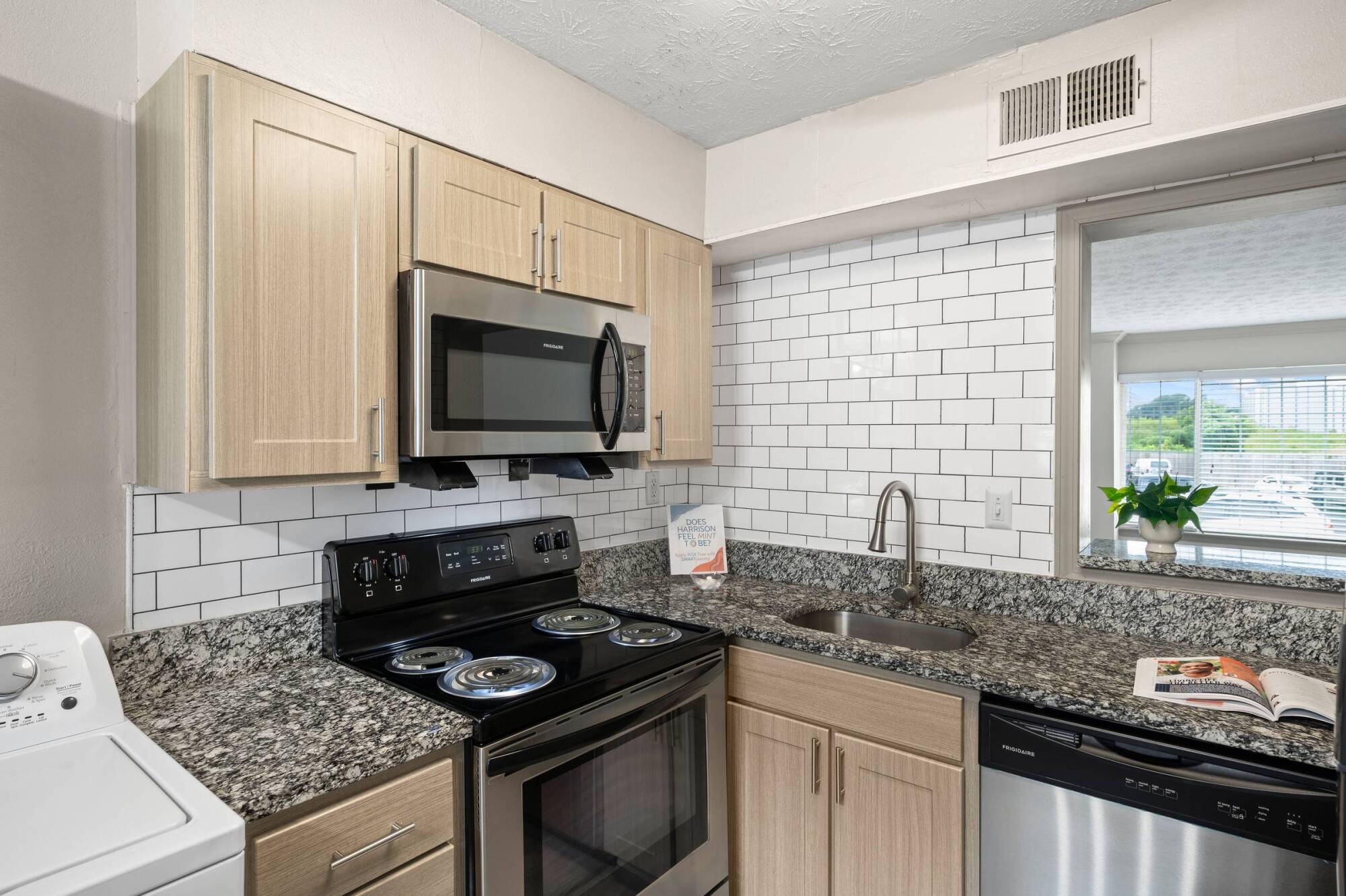 Modern kitchen with light wood cabinets, granite countertops, stainless appliances, and white subway tile backsplash.