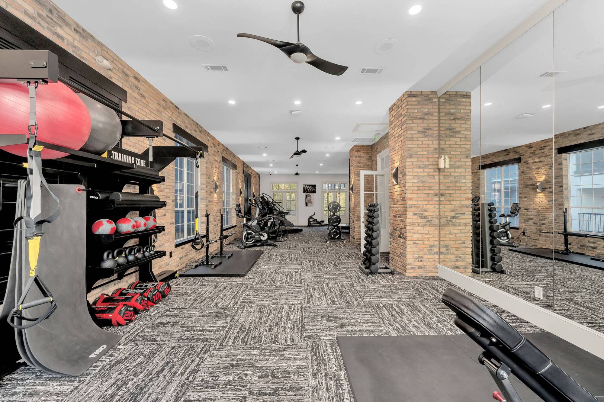 Modern gym with brick walls, various exercise equipment, weights, and large mirrors on one side.