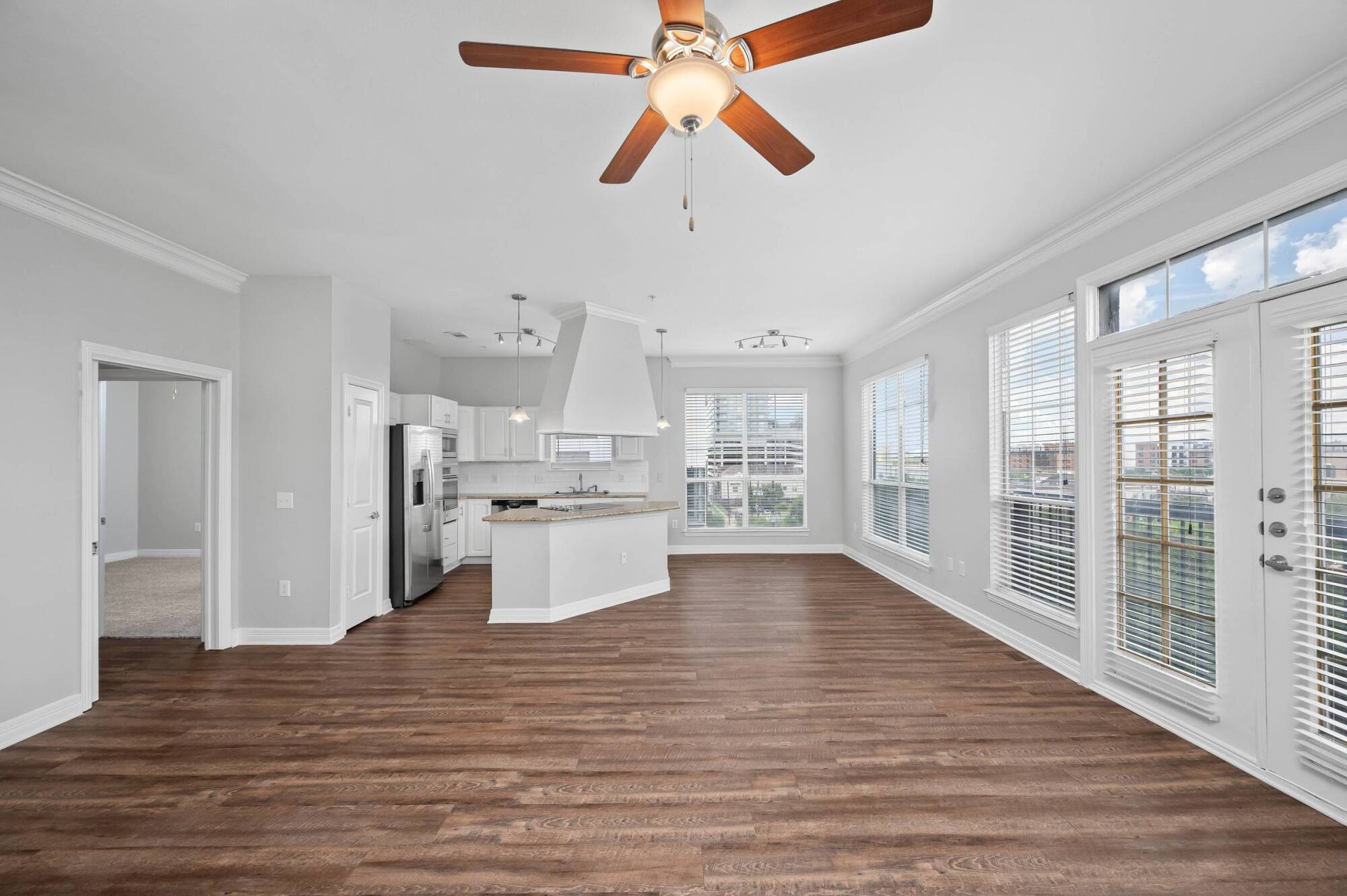 Bright open-plan kitchen and living area with wood floors, large windows, and a ceiling fan.