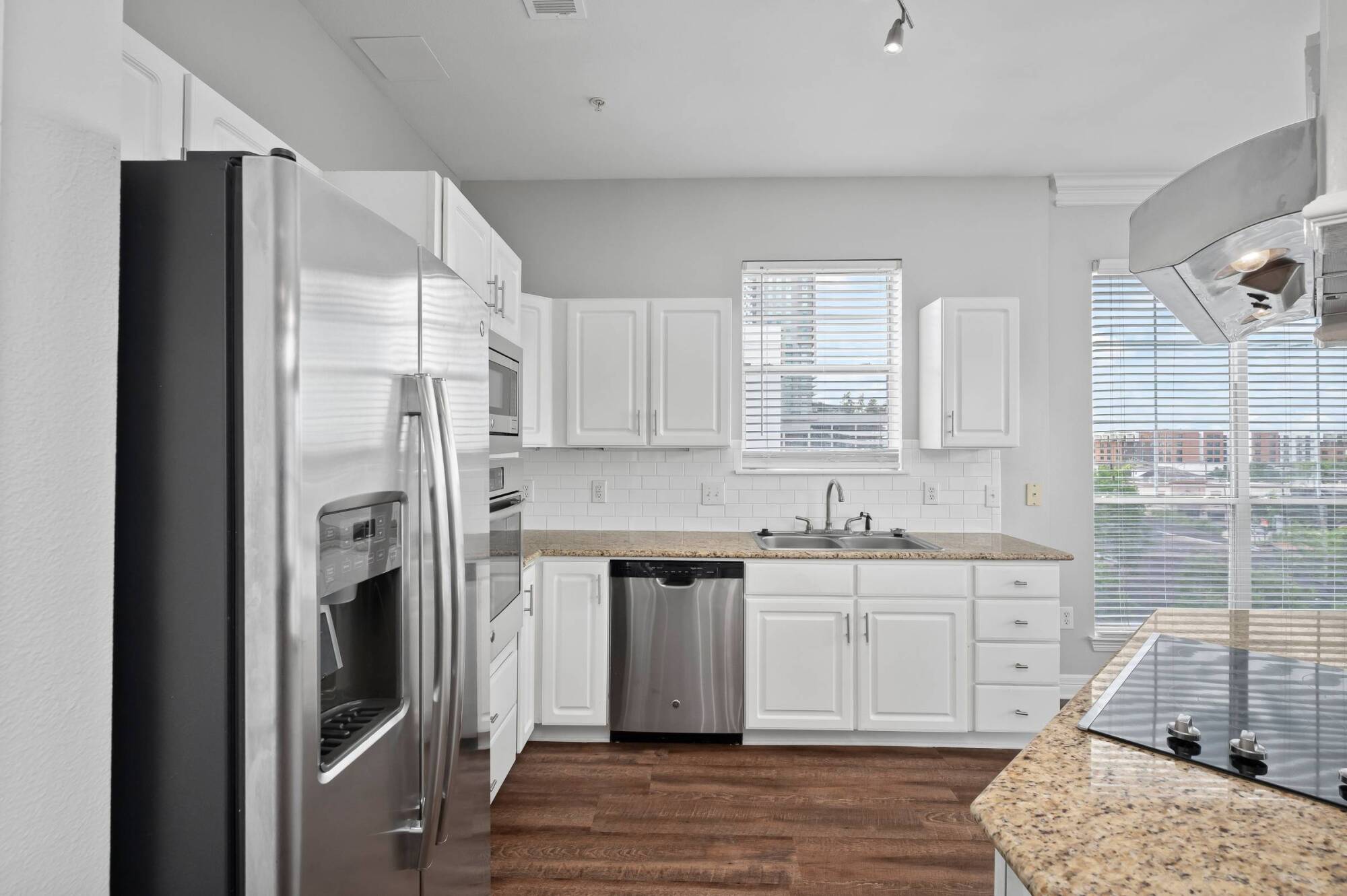 Modern kitchen with white cabinets, stainless steel appliances, granite countertops, and wood flooring.