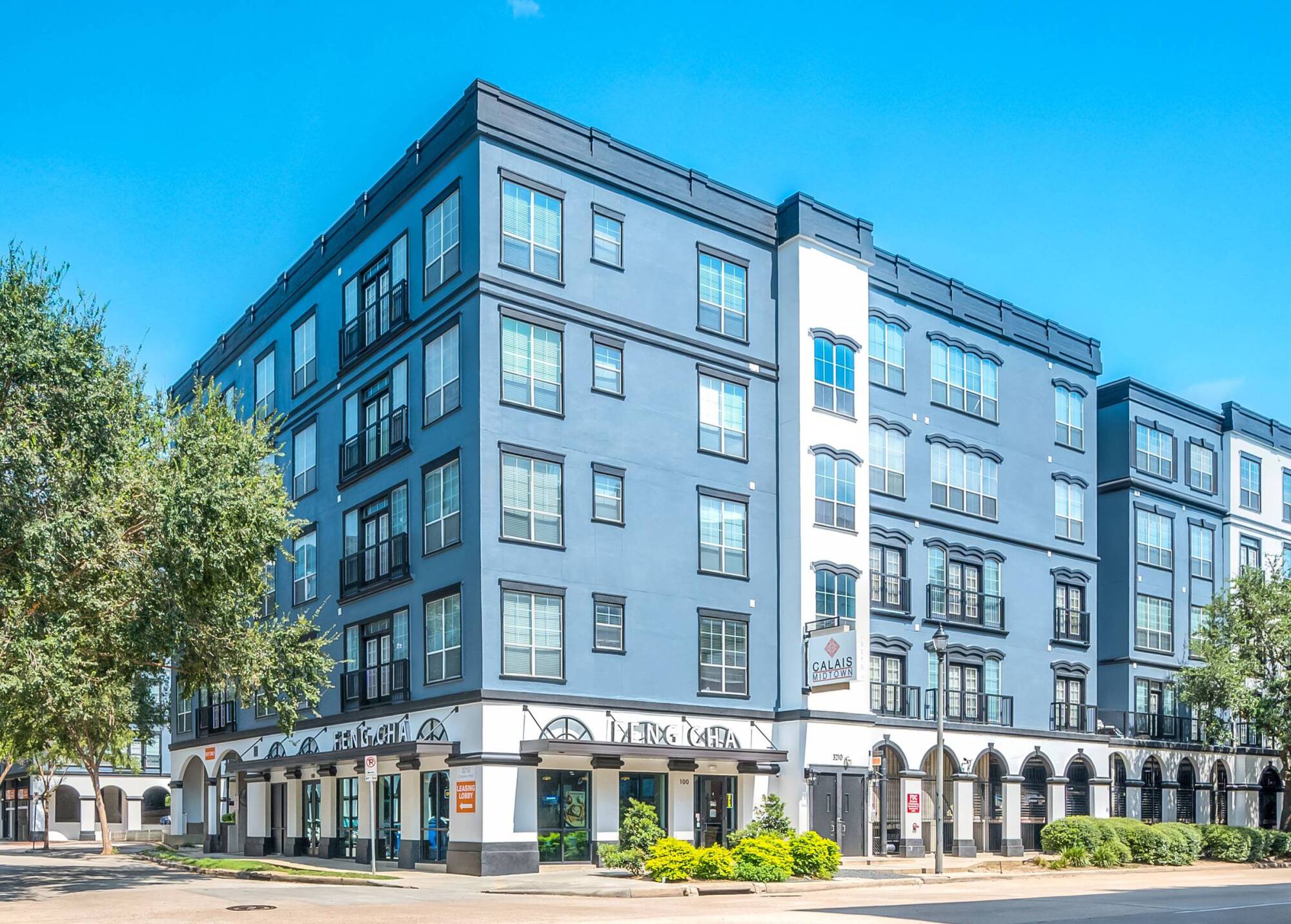 A modern four-story gray apartment building with large windows on a sunny day.