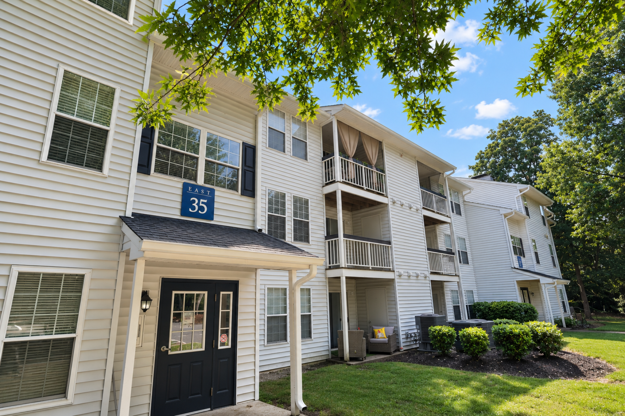 Milestone Apartments White gazebo entrance surrounded by greenery, leading to tennis courts on a sunny day.