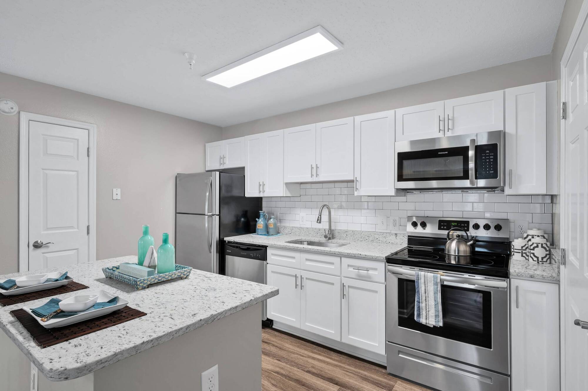 Milestone Apartments Modern kitchen with white cabinets, stainless steel appliances, and a marble island set for two.