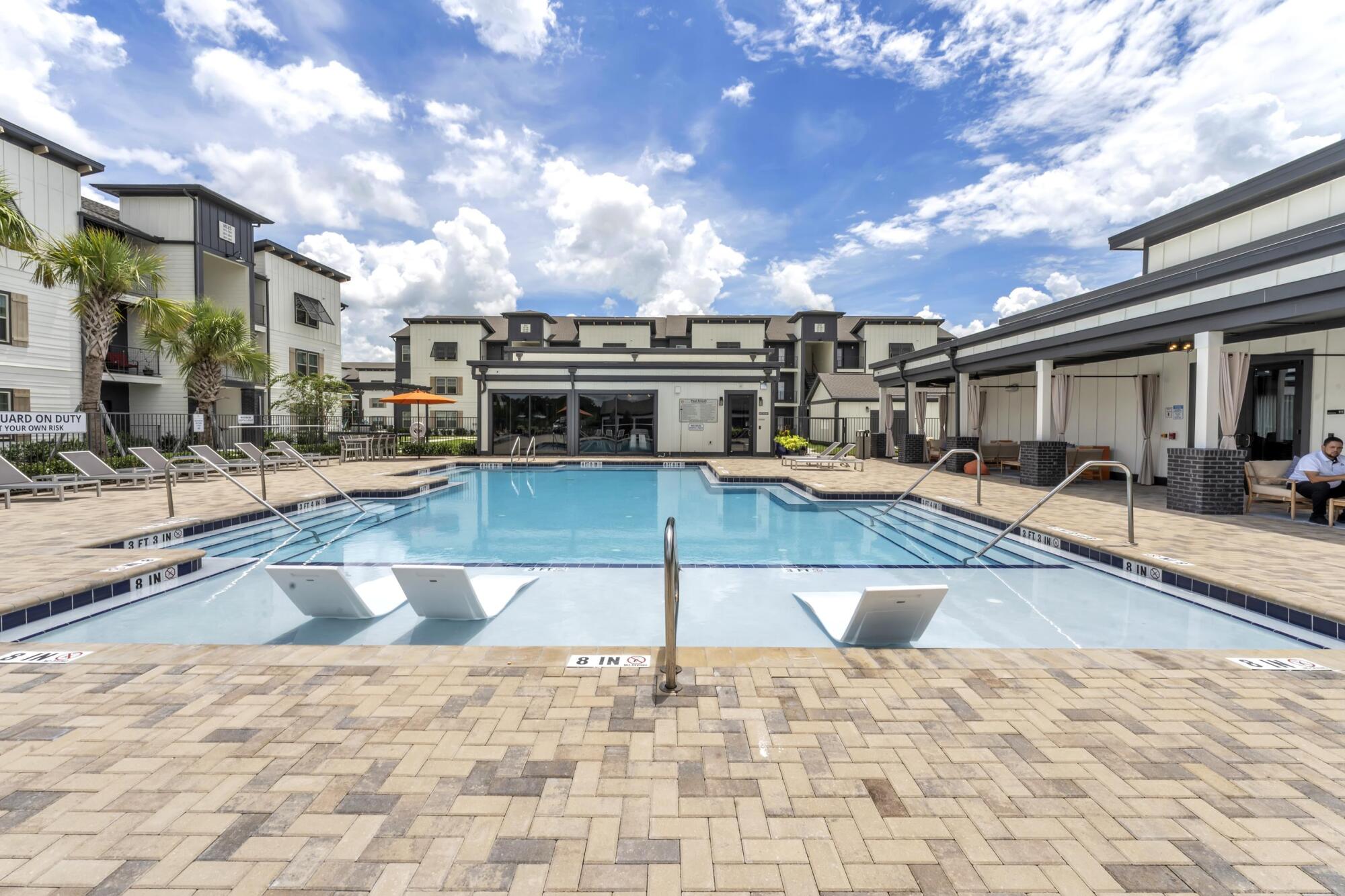Resort-style swimming pool at Pointe Grande Plant City with a sun shelf and view of the apartment exteriors.