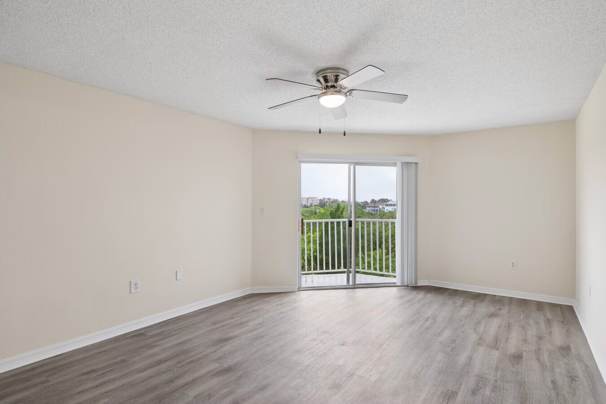 The Landings at Sea Forest apartment living room in New Port Richey, FL with wood-style flooring, a ceiling fan, and balcony access.