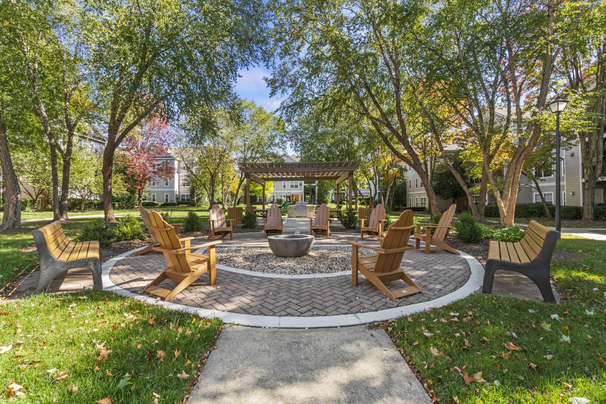 Milestone Apartments Outdoor patio with Adirondack chairs around a fire pit, surrounded by trees and apartment buildings.