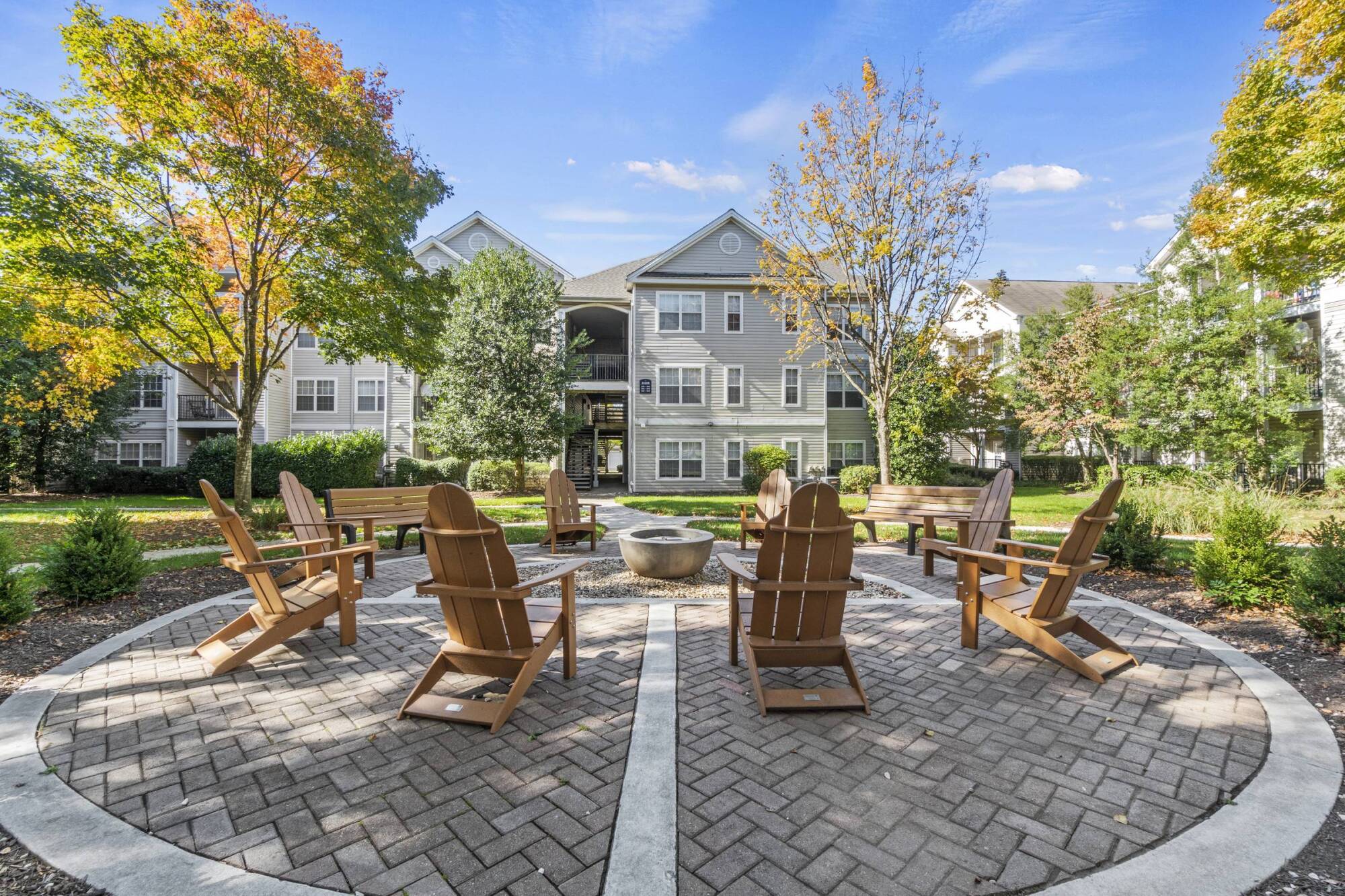 Milestone Apartments Outdoor patio with Adirondack chairs around a fire pit, surrounded by trees and apartment buildings.
