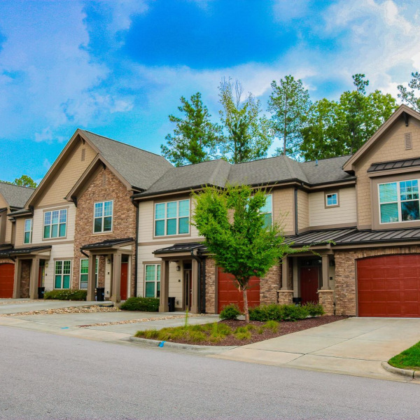 Townhomes at Chapel Watch Village in Chapel Hill, NC, with a row of two-story stone and siding townhomes, red garage doors, and driveways.