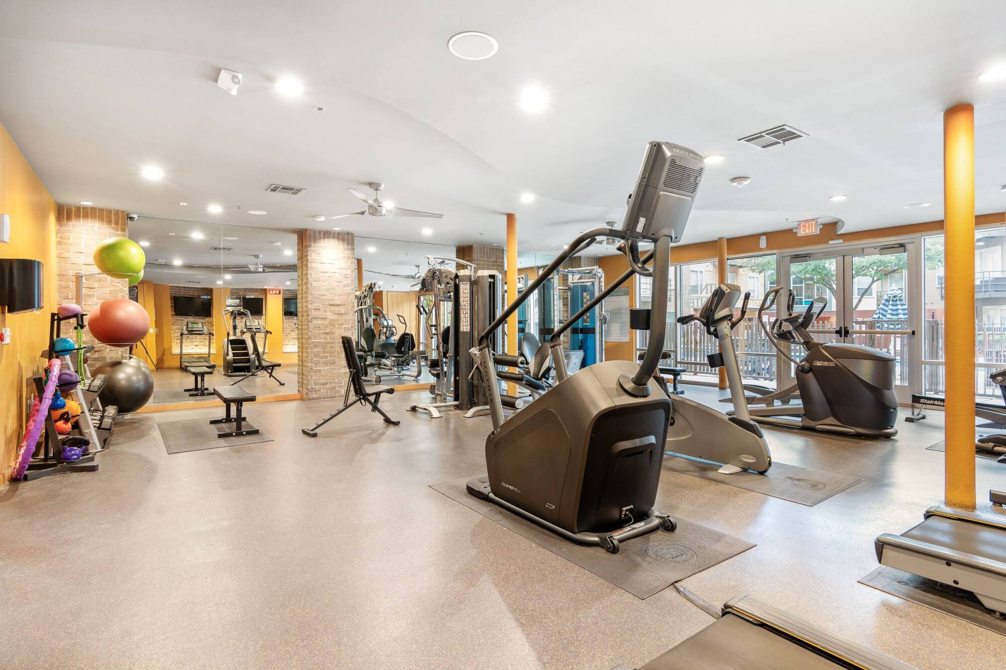 Modern gym with cardio machines, weight equipment, benches, and TVs in a bright, spacious room.