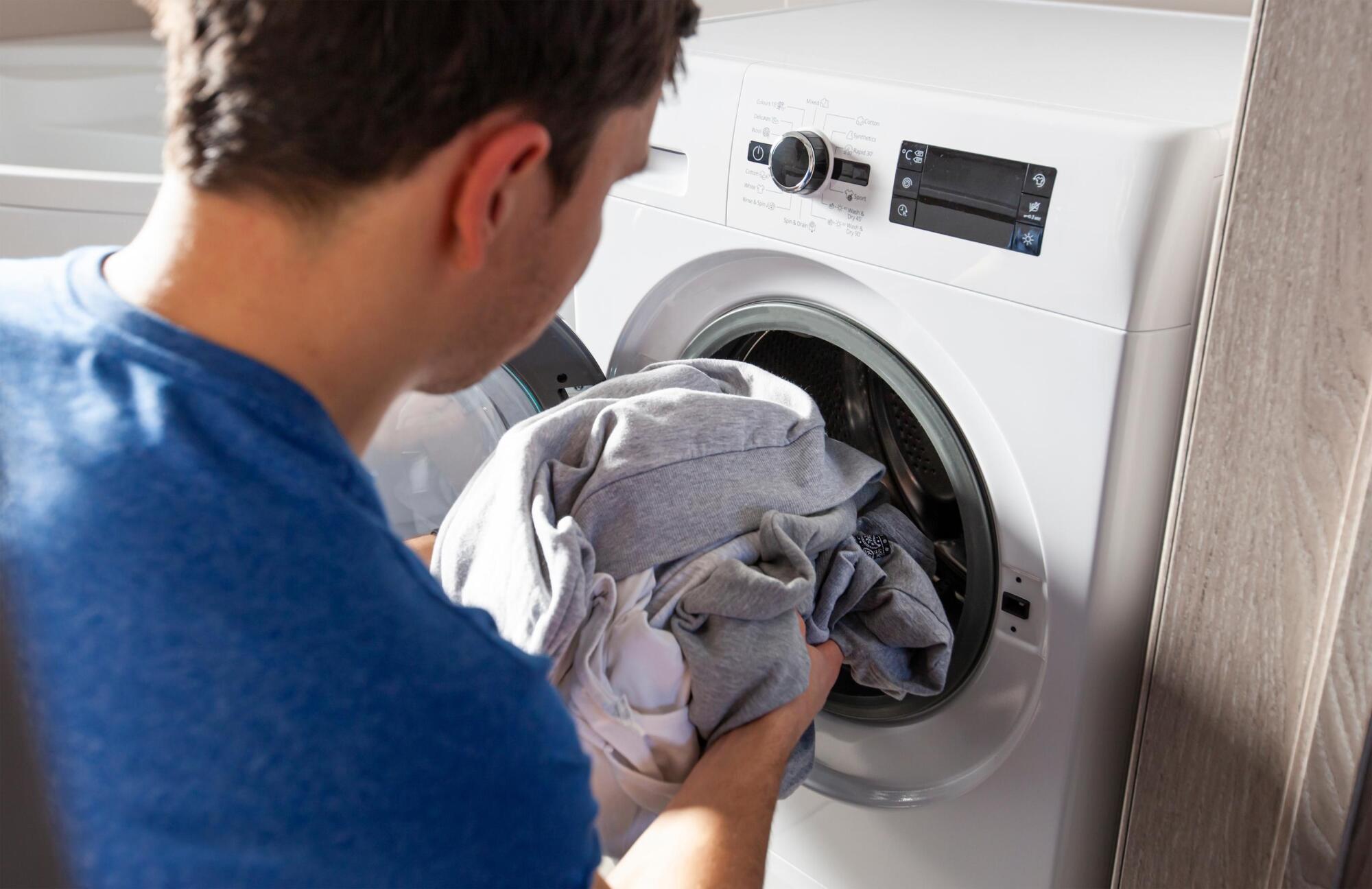 Close-up of a person loading a modern front-loading washer and dryer located inside the apartment.