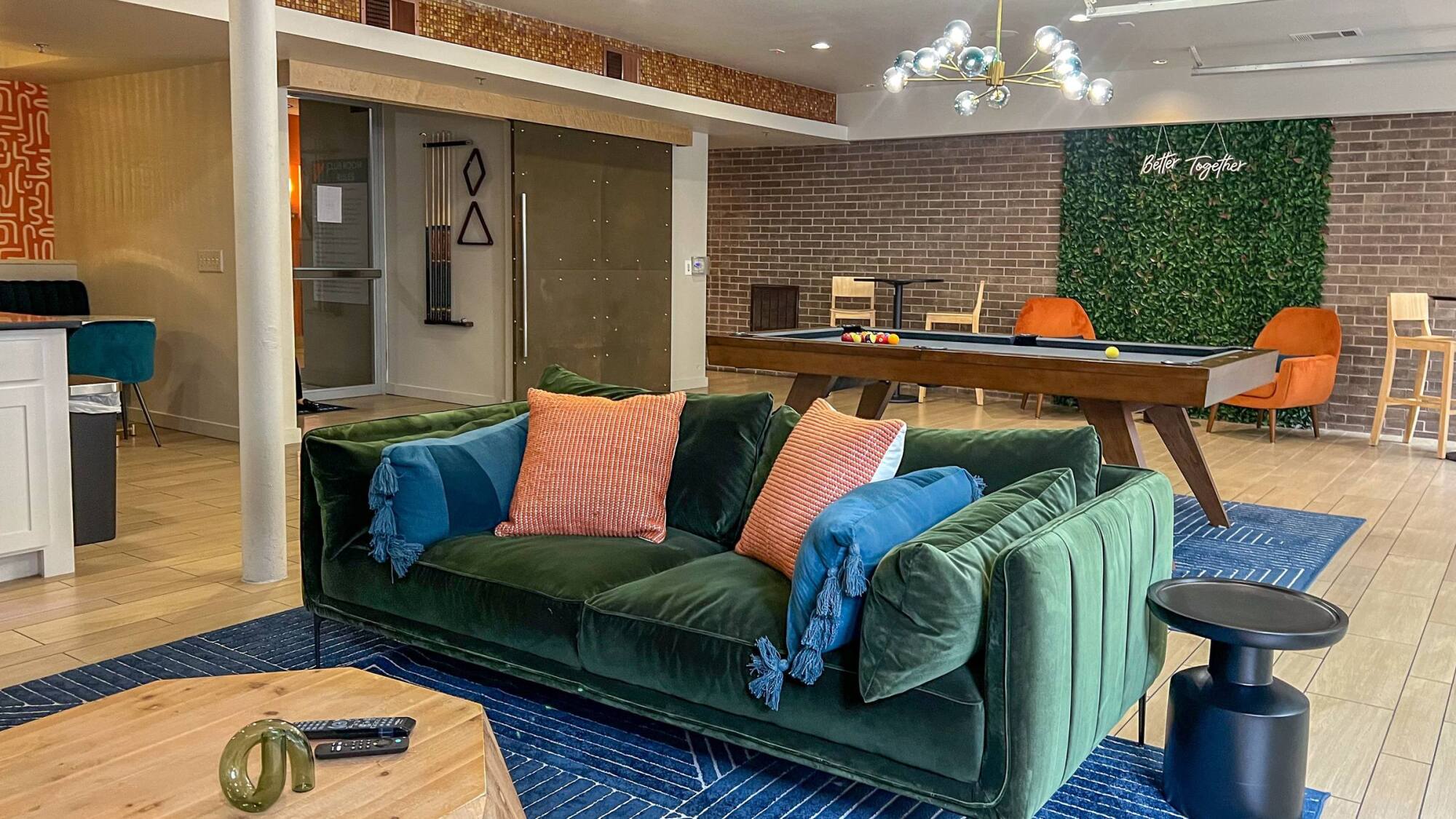 Modern lounge with a green velvet sofa, pool table, bar stools, and decorative wall greenery.