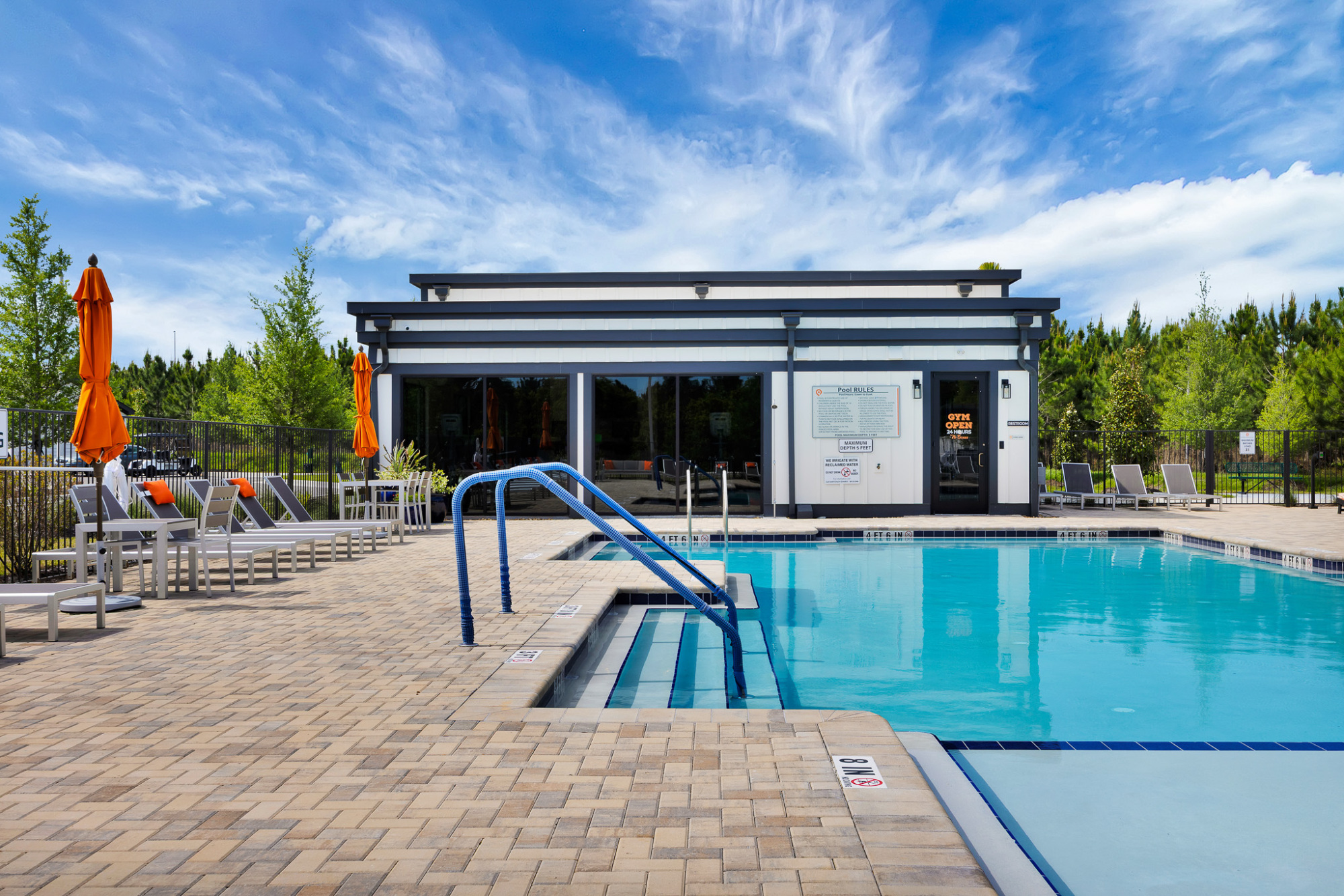 Large outdoor swimming pool with lounge seating and a modern clubhouse in the background.