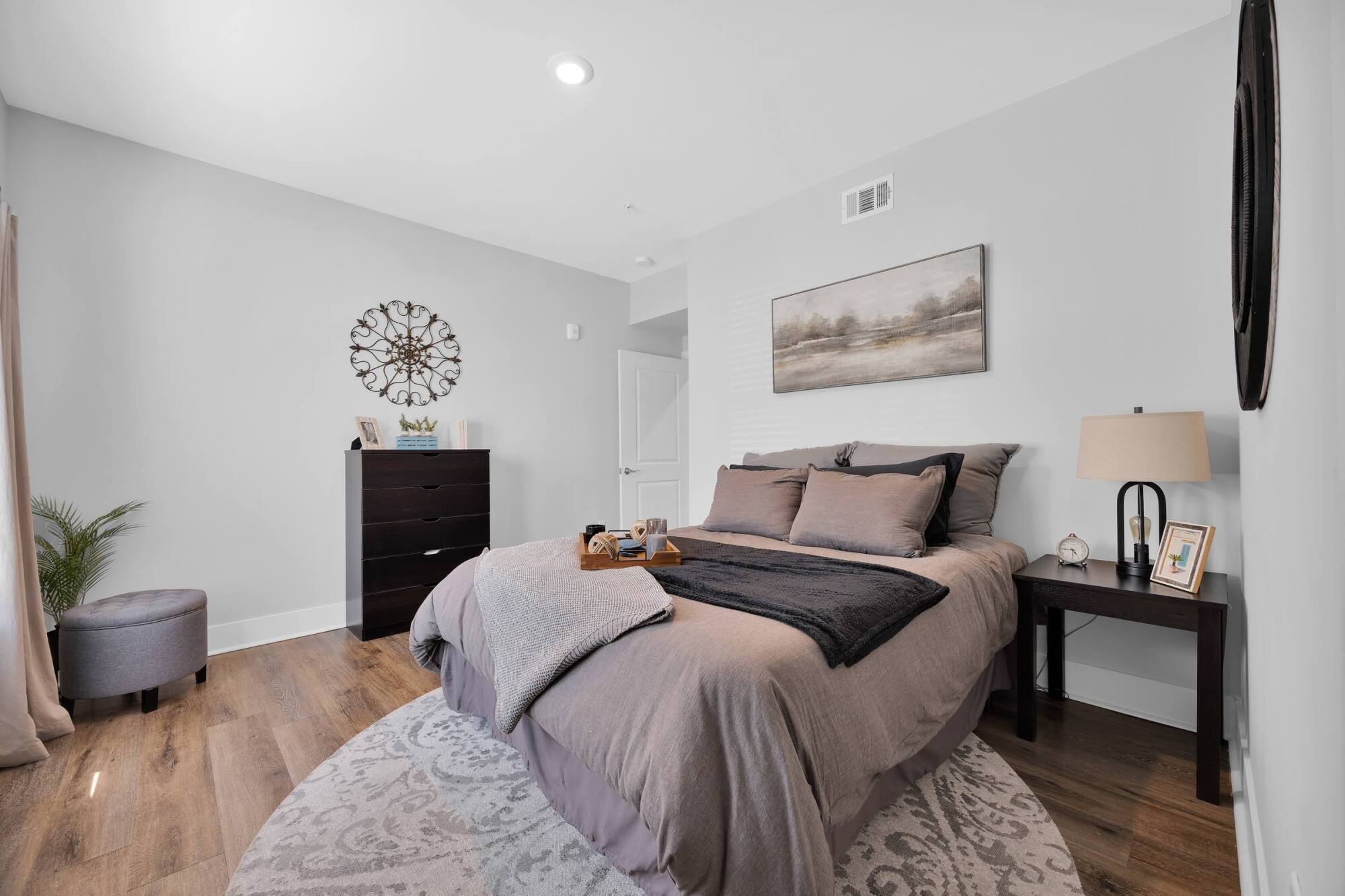 A cozy bedroom with a made bed, bedside table, dresser, and neutral décor in soft gray and beige tones.
