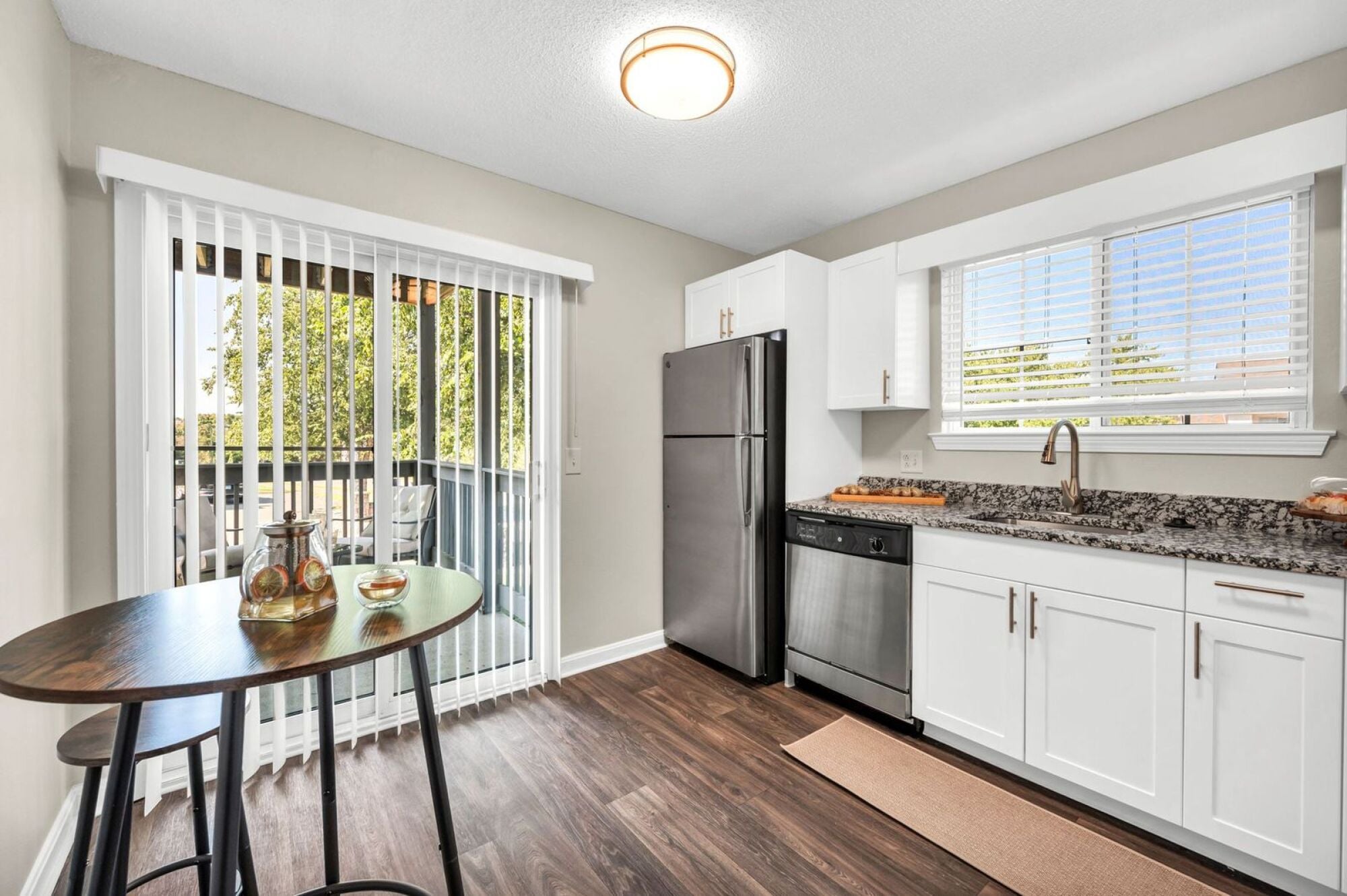 Milestone Apartments Modern kitchen with white cabinets, stainless steel appliances, and a marble island set for two.