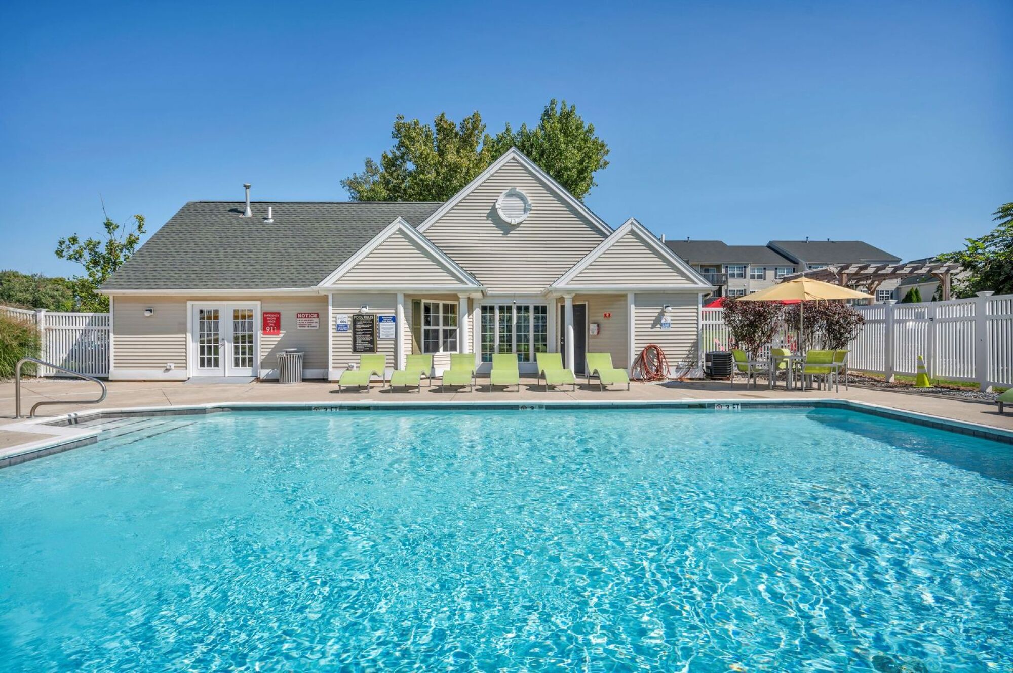 Outdoor swimming pool with lounge chairs in front of a clubhouse on a sunny day.