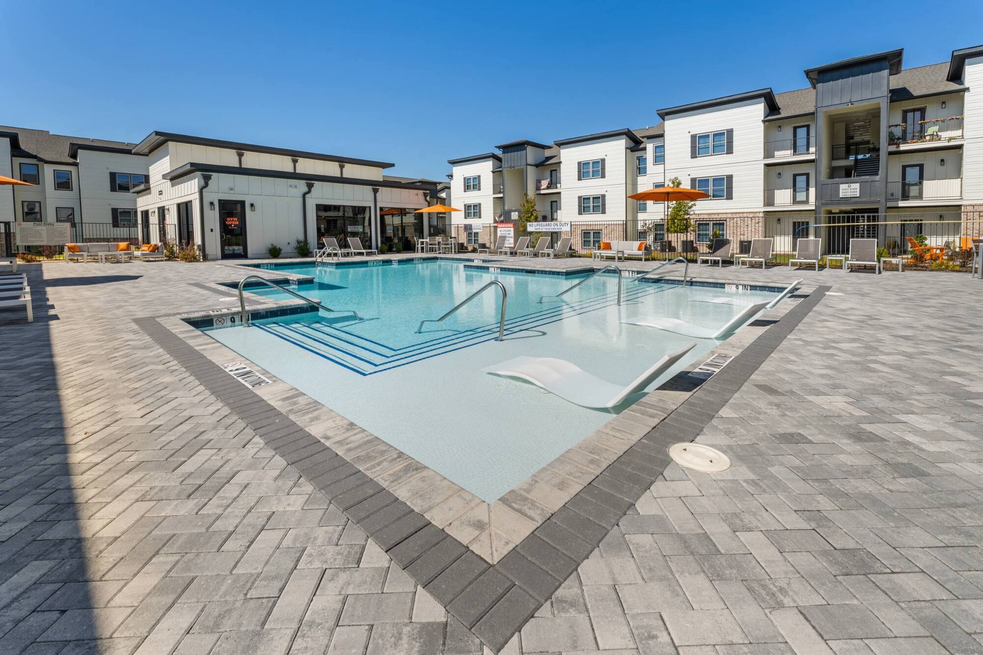 Community pool with shallow lounging area, steps, and modern surroundings