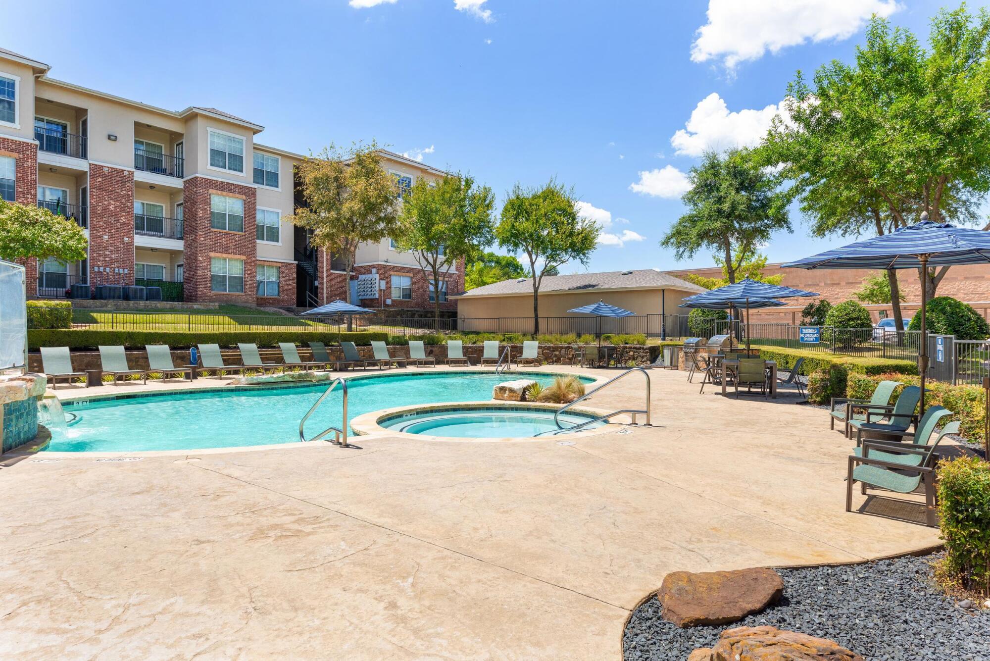 Swimming pool and spa at Bella Ruscello in Duncanville, TX with sundeck lounge chairs, umbrellas, and mature shade trees