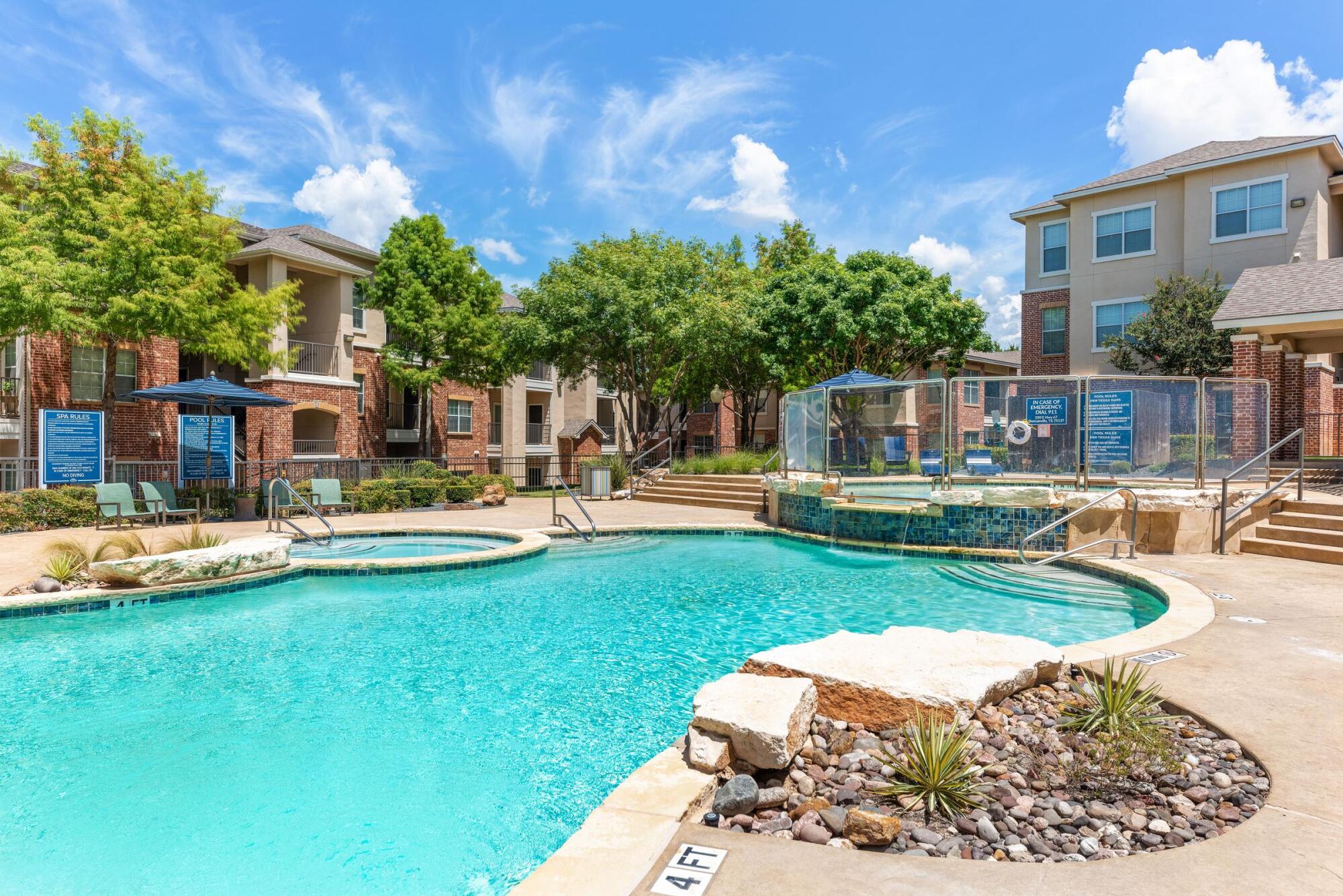 Sparkling swimming pool with natural stone features and hot tub at Bella Ruscello apartments in Duncanville, TX