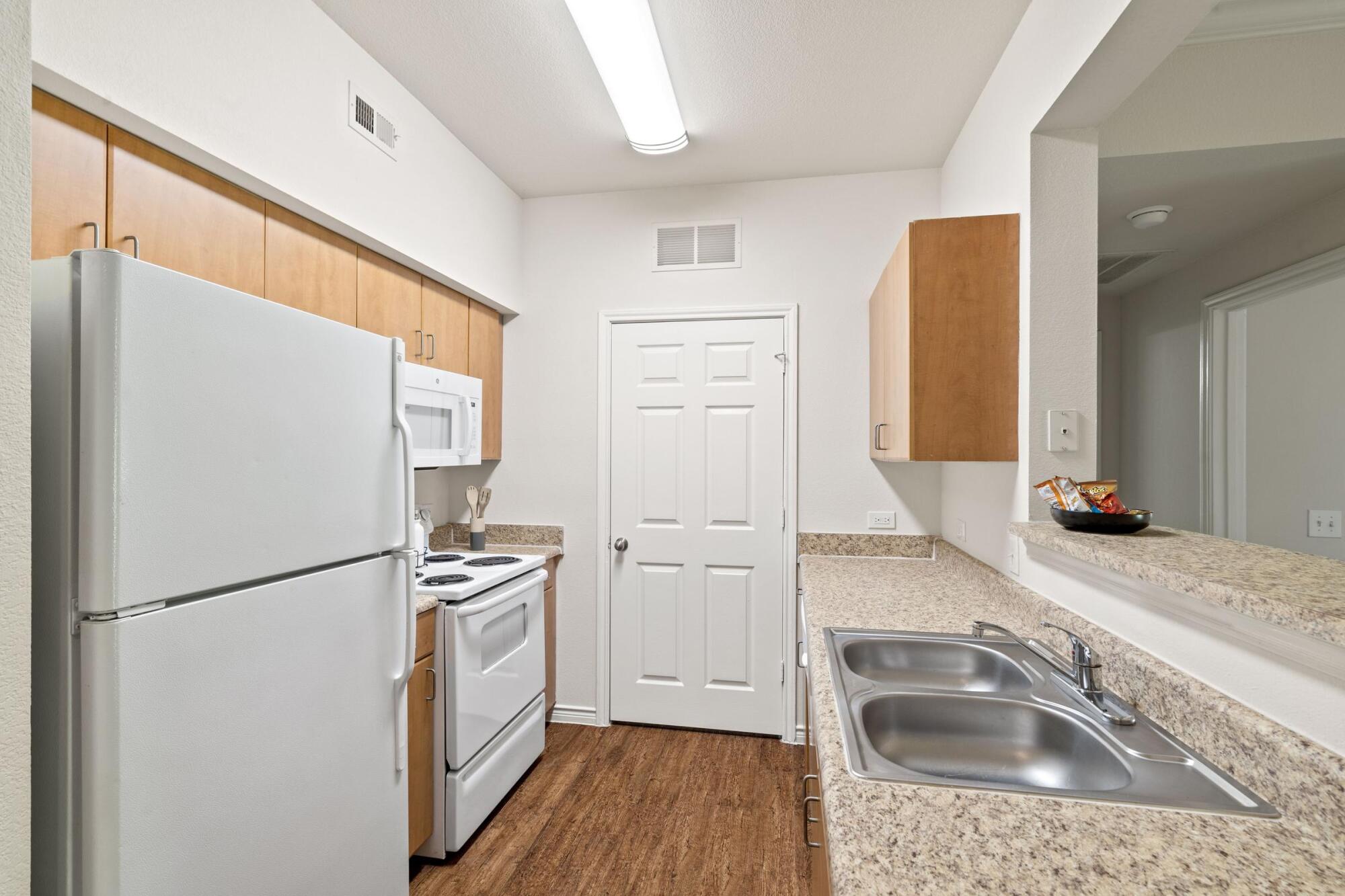 Galley kitchen at Bella Ruscello apartments in Duncanville, TX with white appliances, granite counters, and a double sink