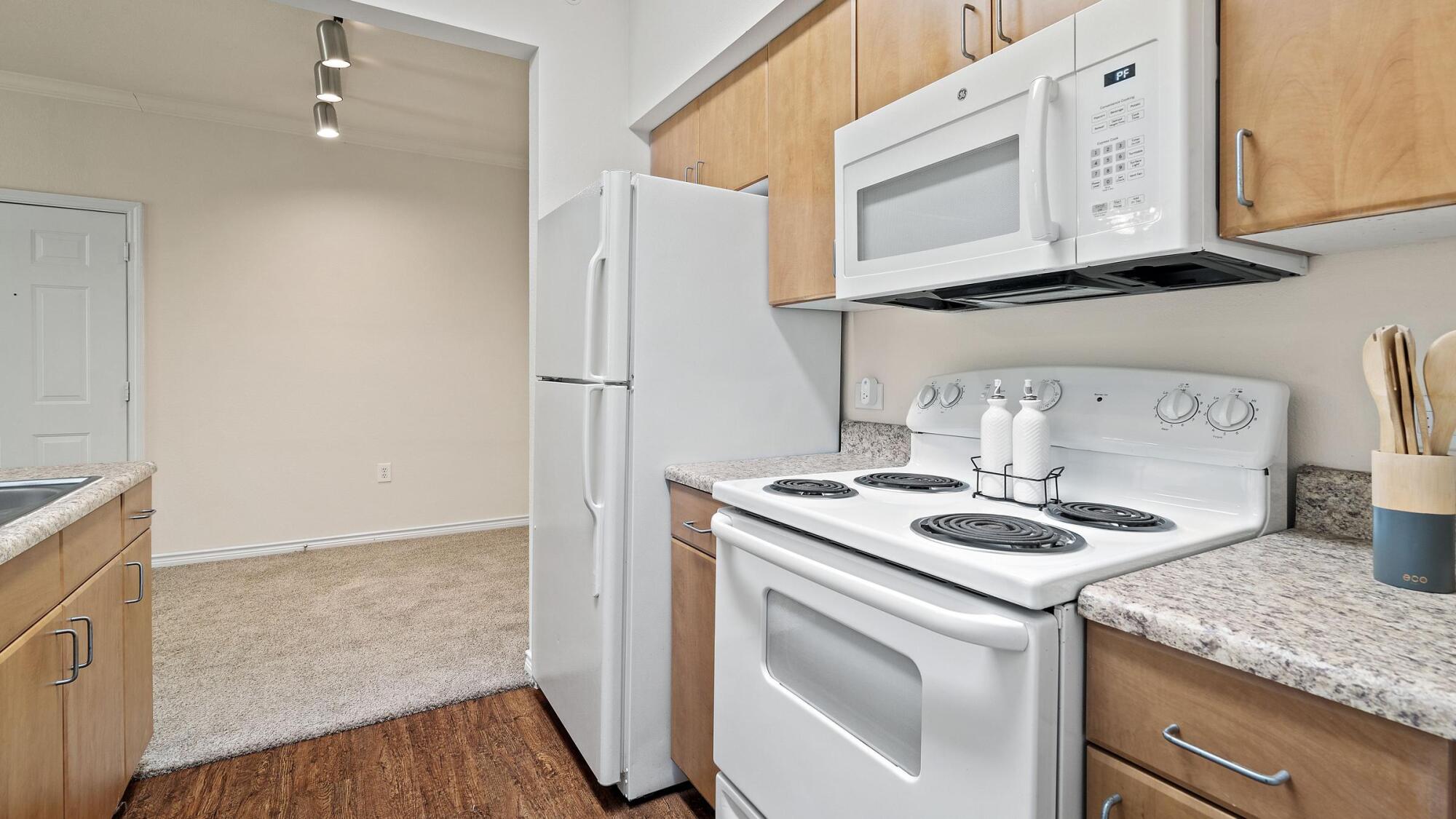 Bella Ruscello apartment kitchen in Duncanville, TX with white appliances, light wood cabinets, and granite countertops
