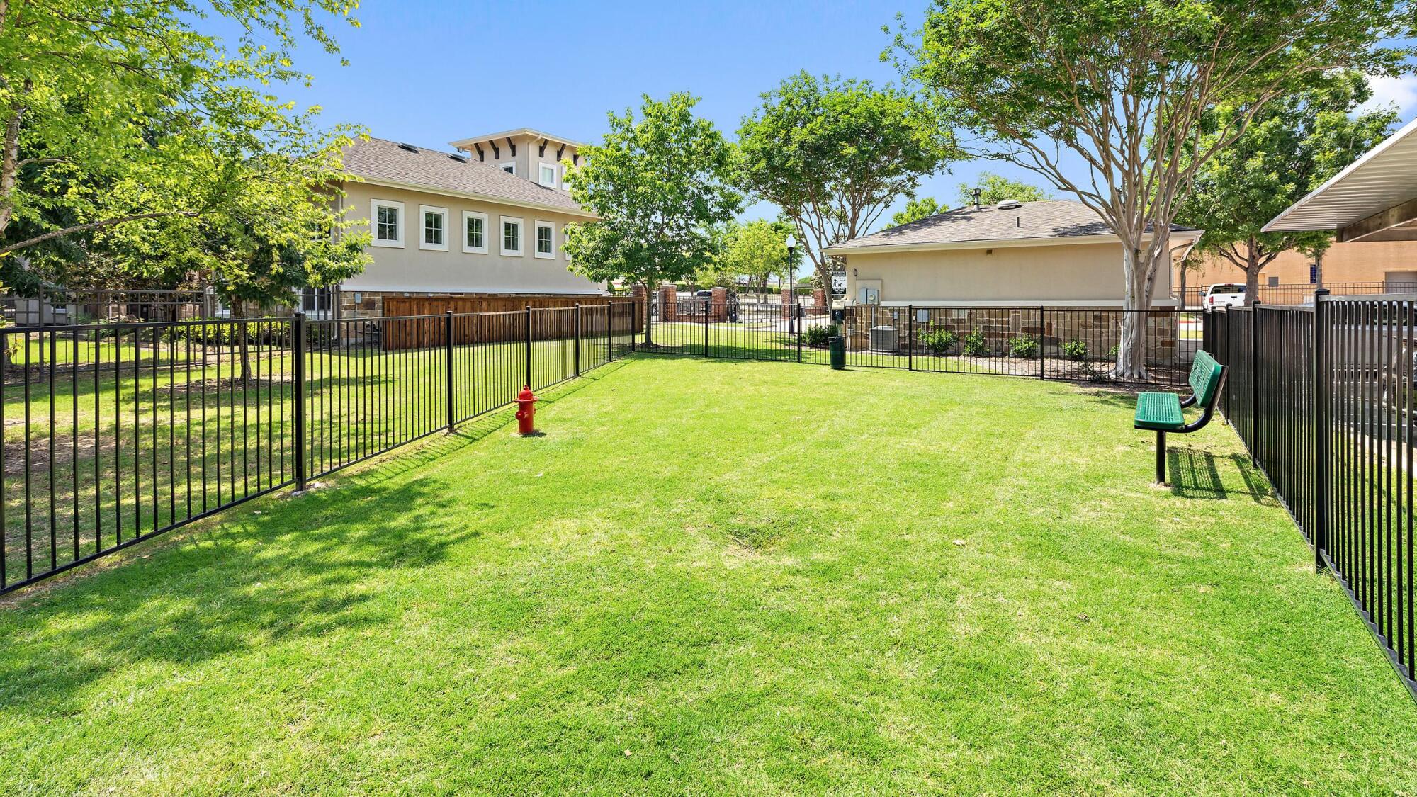 Fenced dog park at Bella Ruscello in Duncanville, TX with green grass, a red fire hydrant, and mature shade trees