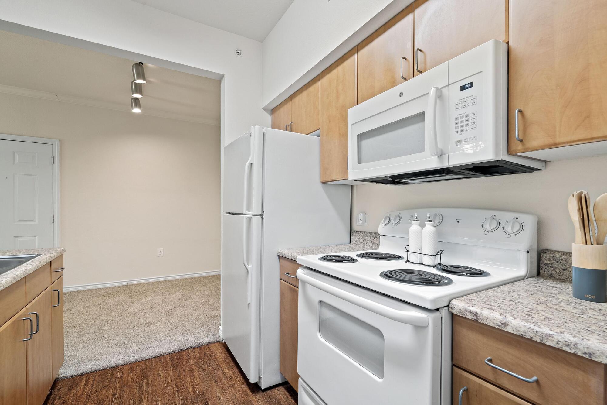 Apartment kitchen at Bella Ruscello in Duncanville, TX with white appliances, wood cabinets, granite countertops, and adjacent dining area