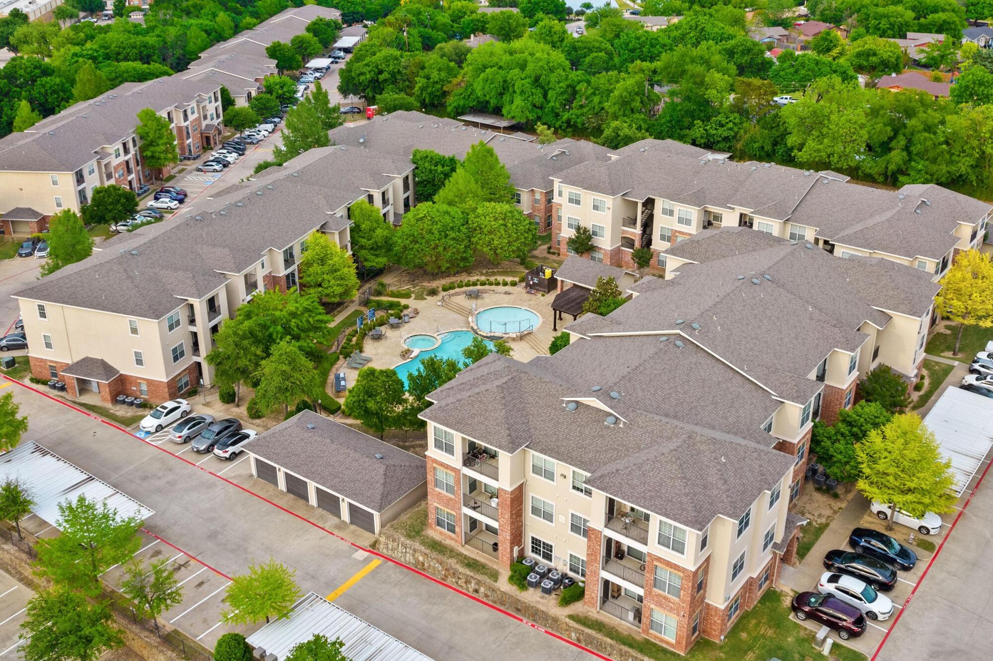 Aerial view of Bella Ruscello apartments in Duncanville, TX with resort-style pool, lush landscaping, and brick and stucco buildings