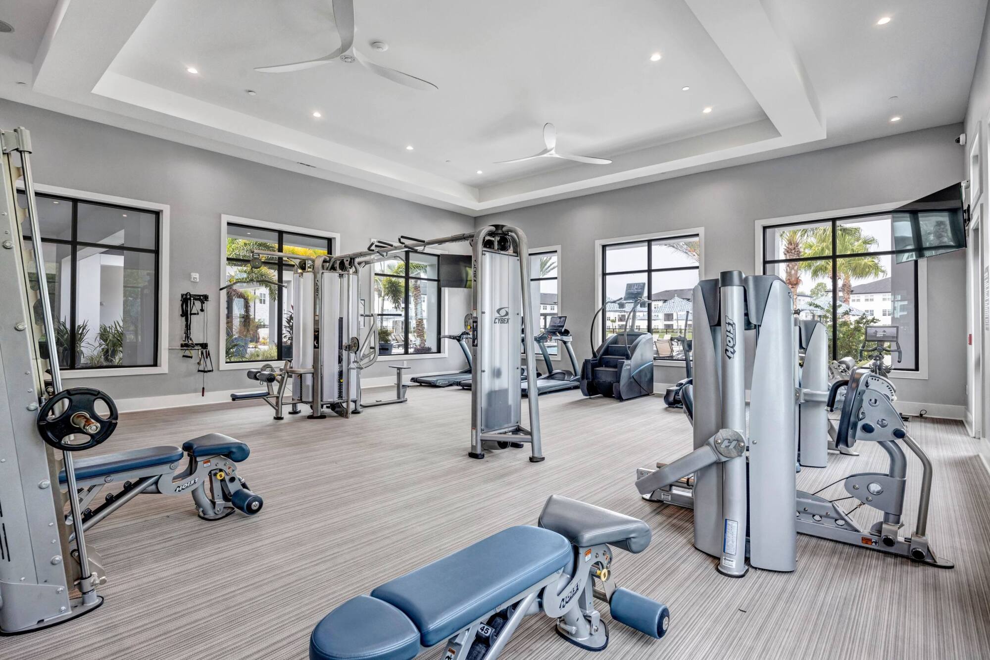 Modern gym with various exercise machines and benches, large windows, and bright, spacious interior.
