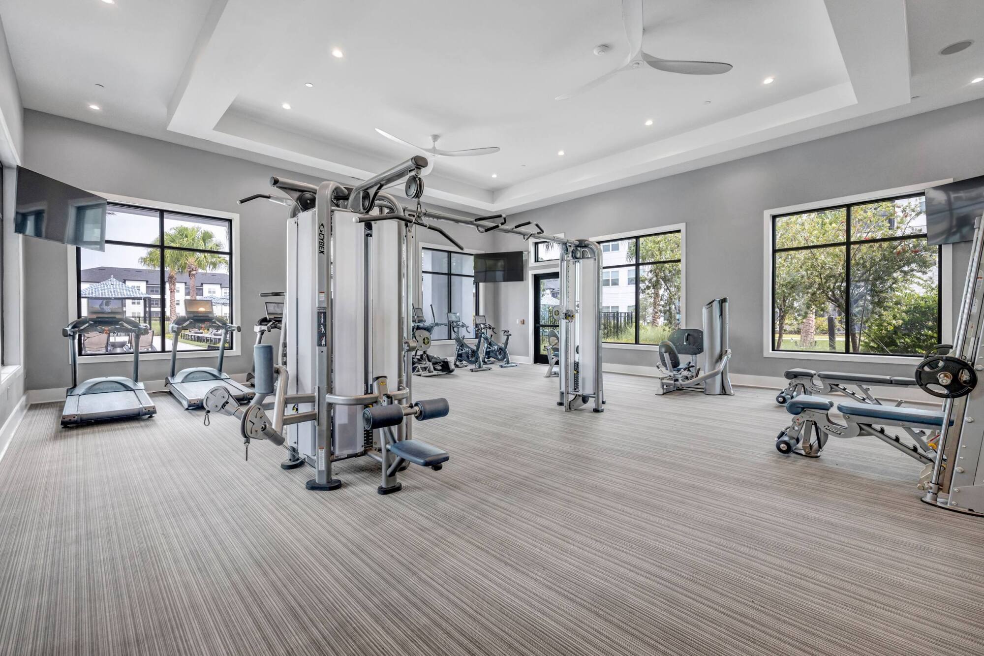 Modern gym with various exercise machines, treadmills, and large windows letting in natural light.
