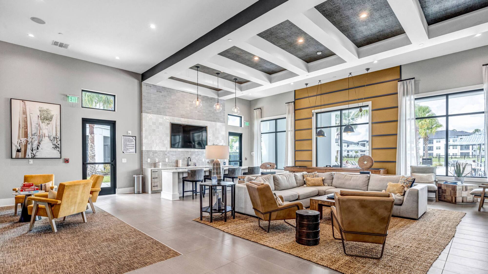 Modern lounge with sofas, chairs, and large windows letting in natural light, decorated in neutral tones.