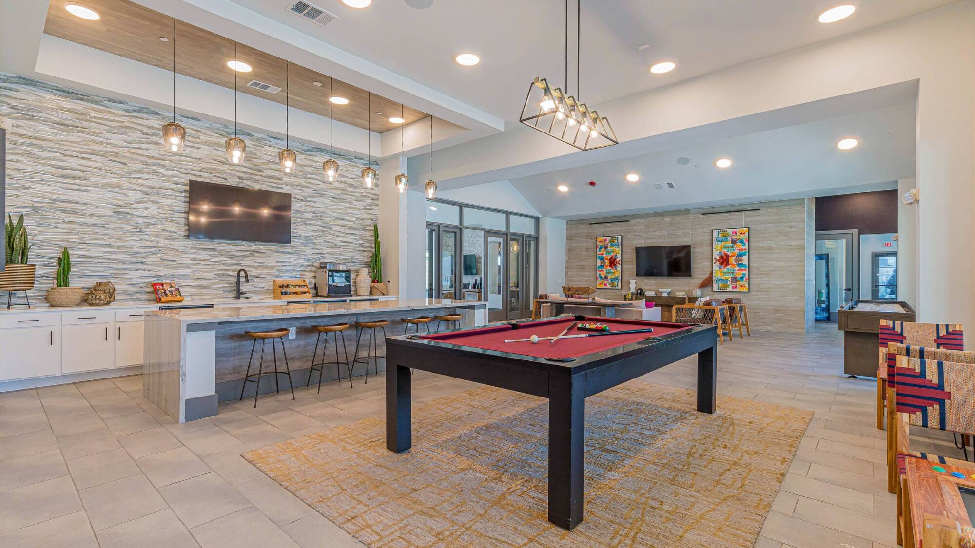 Modern game room with a pool table, bar seating, TV, and stylish decor under bright ceiling lights.