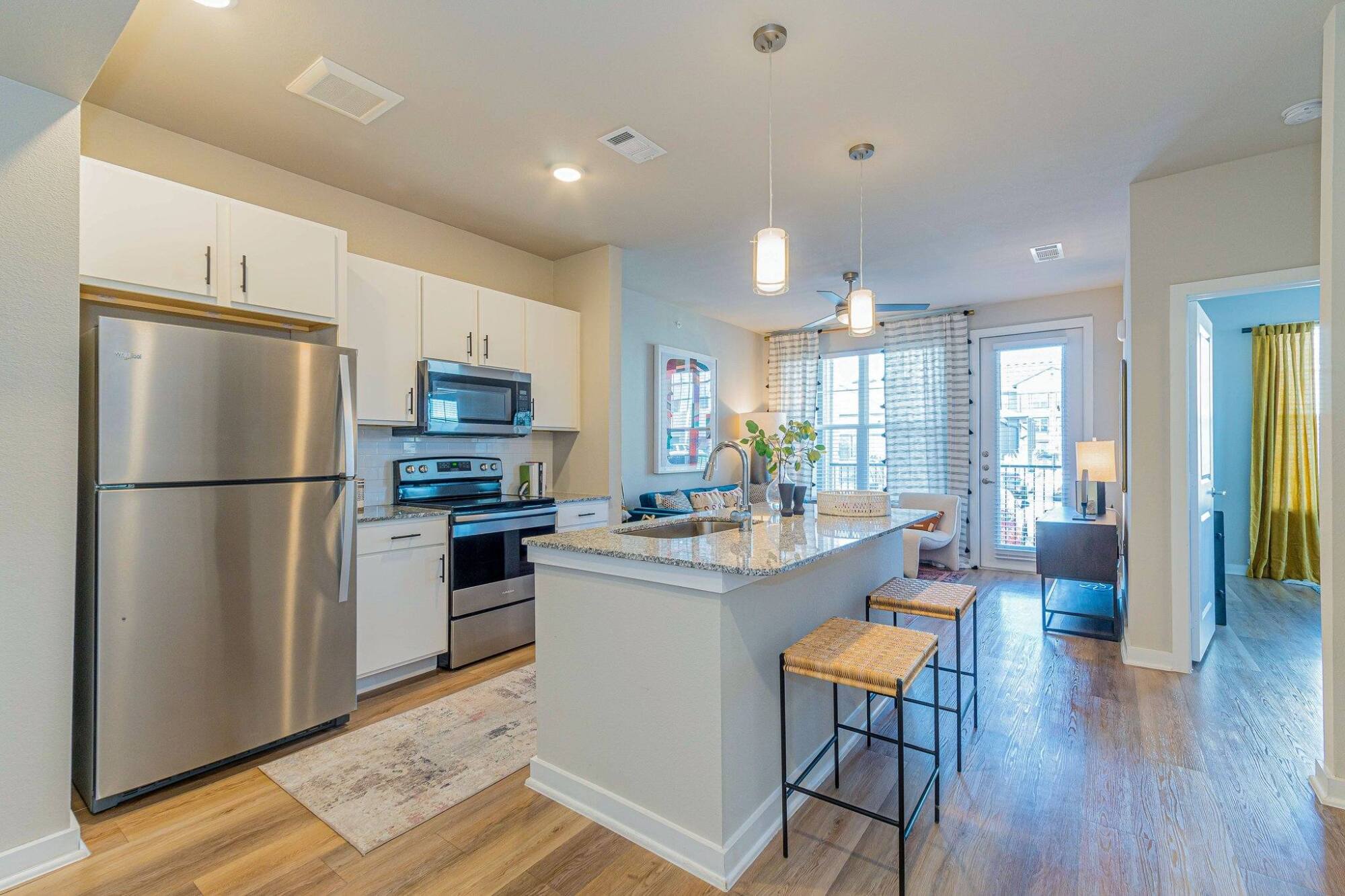 Modern kitchen with stainless steel appliances, island with seating, and bright dining area in the background.