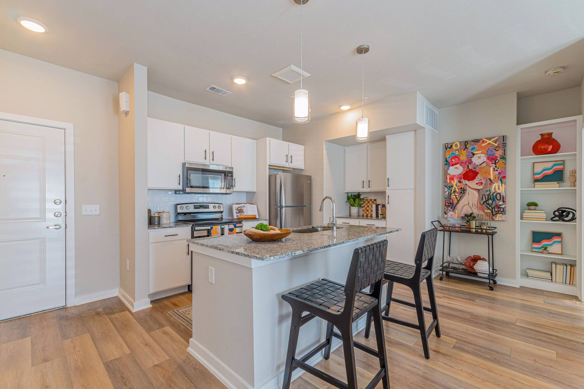 Modern kitchen with white cabinets, stainless steel appliances, island seating, and colorful wall art.