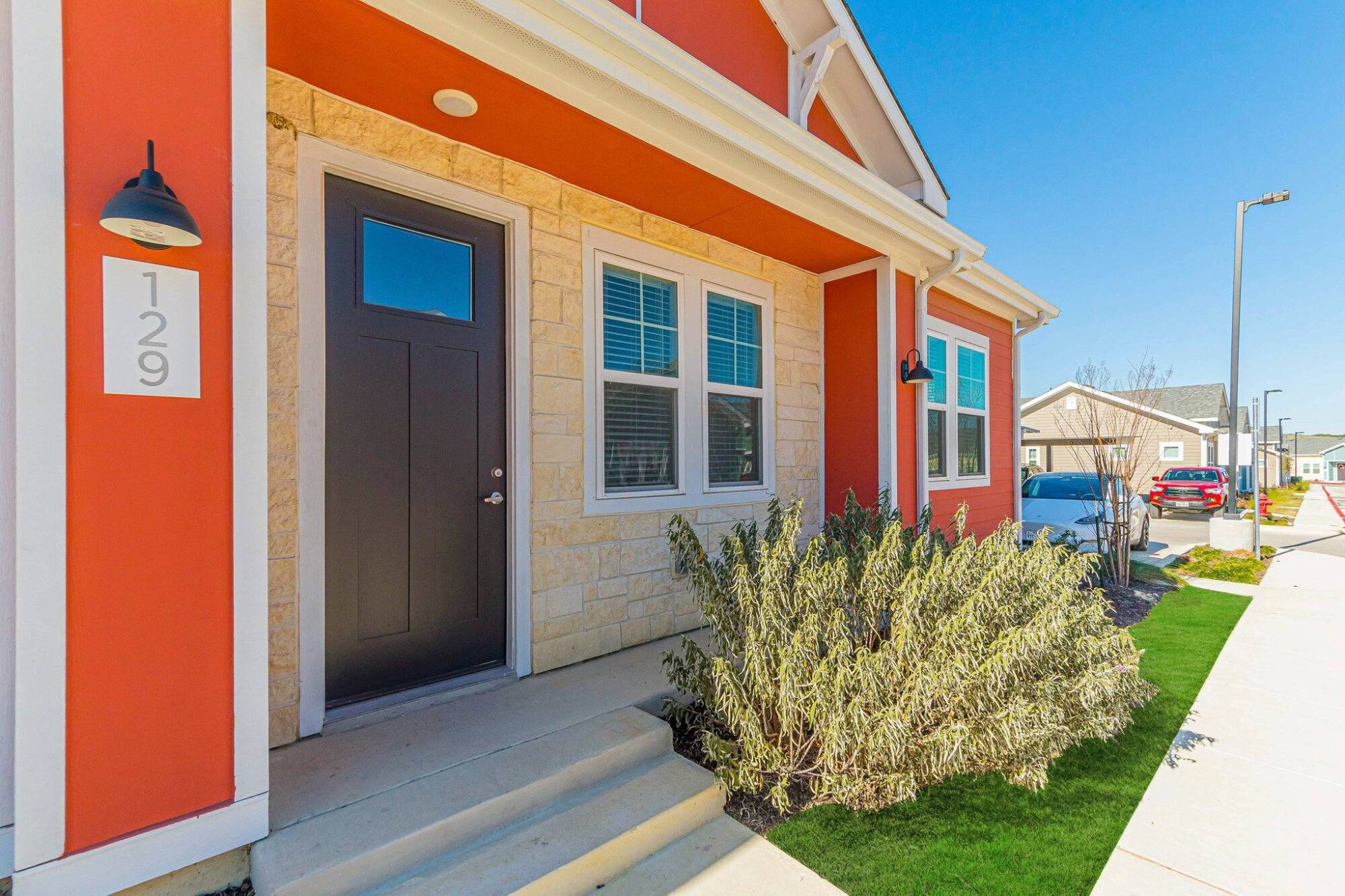 Front entrance of a house with an orange exterior, stone trim, black door, and a small shrub by the steps.