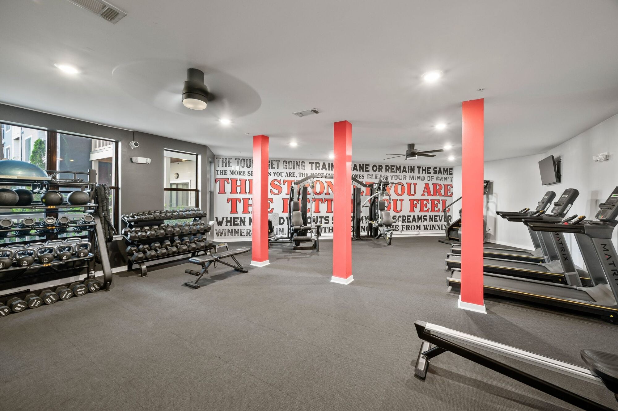 Modern gym with treadmills, weight machines, free weights, large mirrors, and motivational wall art.