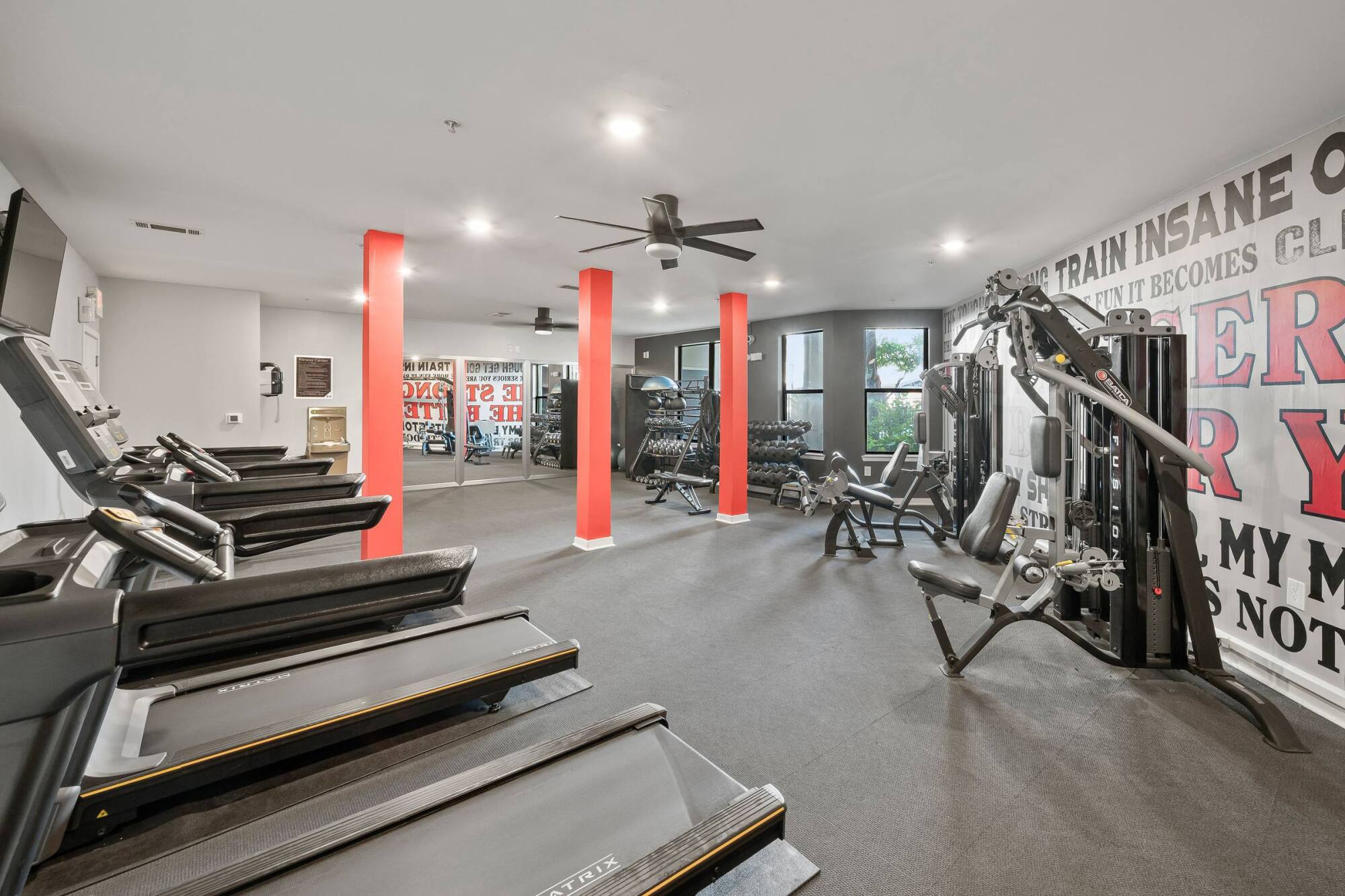 Modern gym with treadmills, weight machines, free weights, large mirrors, and motivational wall art.