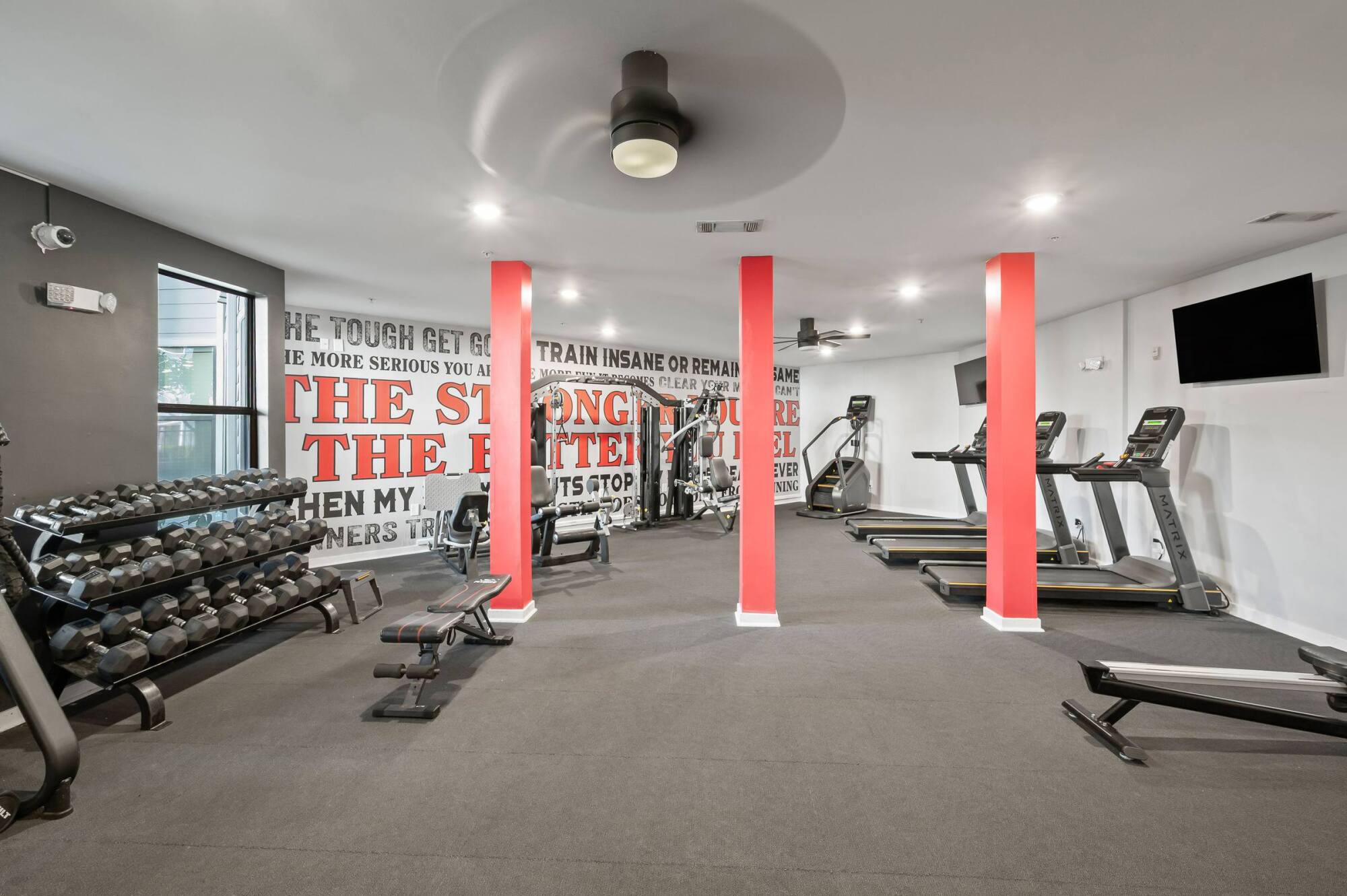 Modern gym room with treadmills, weight racks, benches, and motivational quotes on the wall.