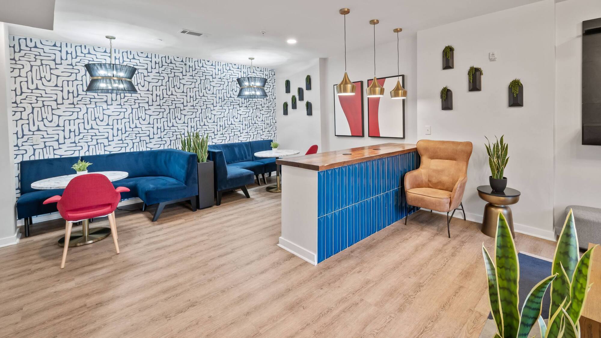 Modern lounge with blue sofas, marble tables, gold lights, plants, and geometric wall art on wood flooring.