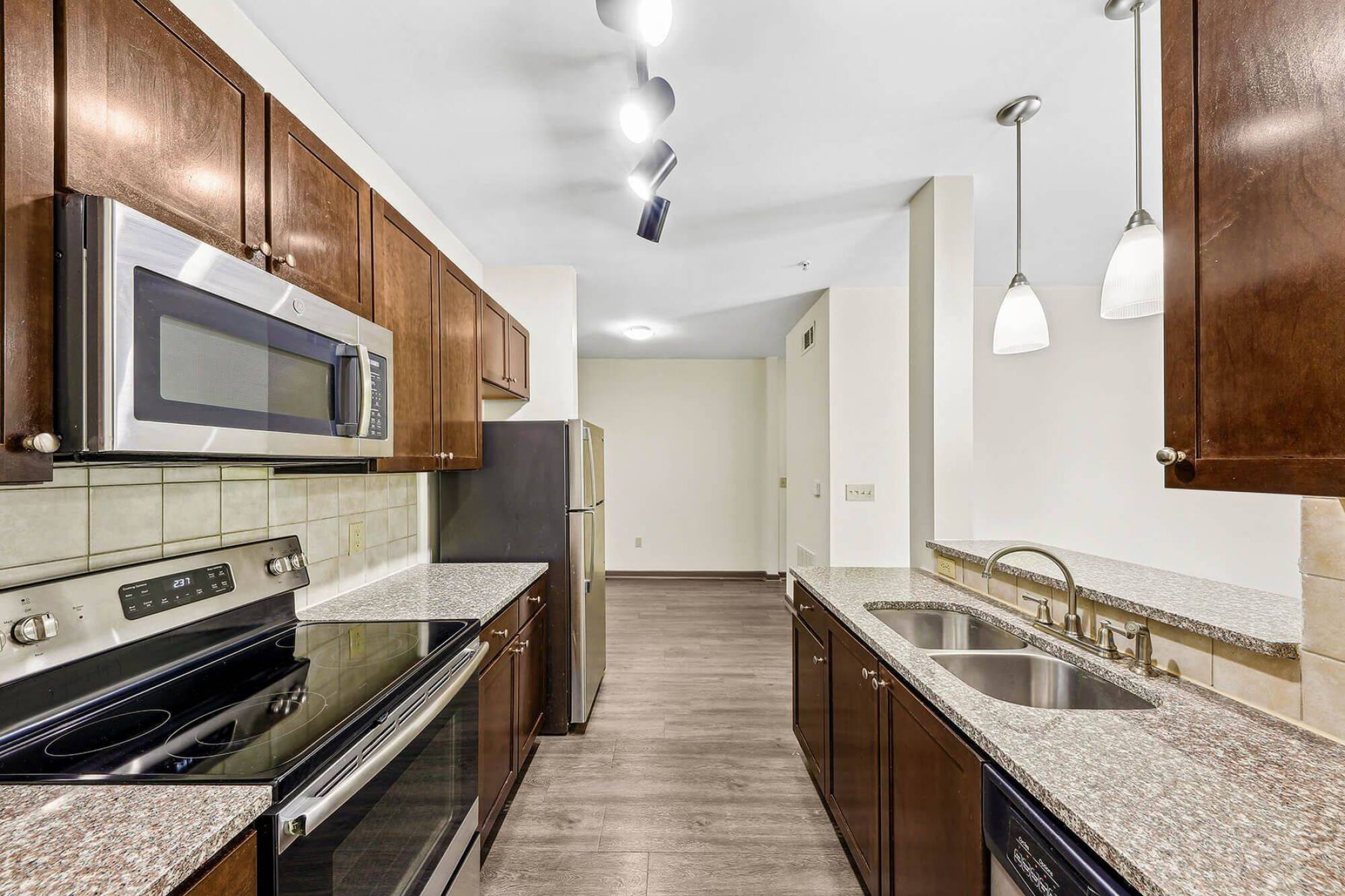 Modern kitchen with stainless steel appliances, granite countertops, and dark wood cabinets under bright lighting.