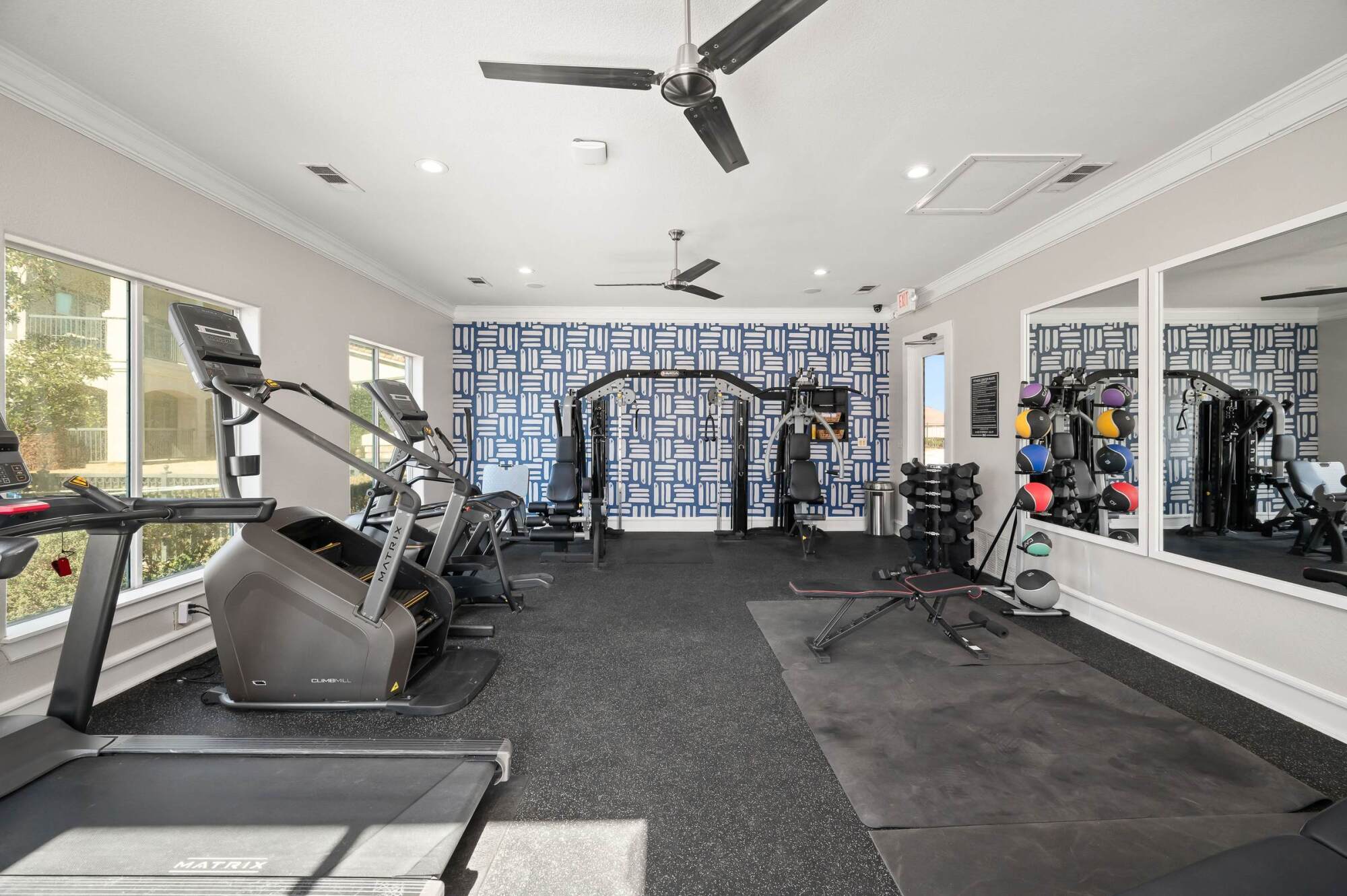 Modern gym with treadmills, weight machines, free weights, benches, mirrors, and a geometric accent wall.