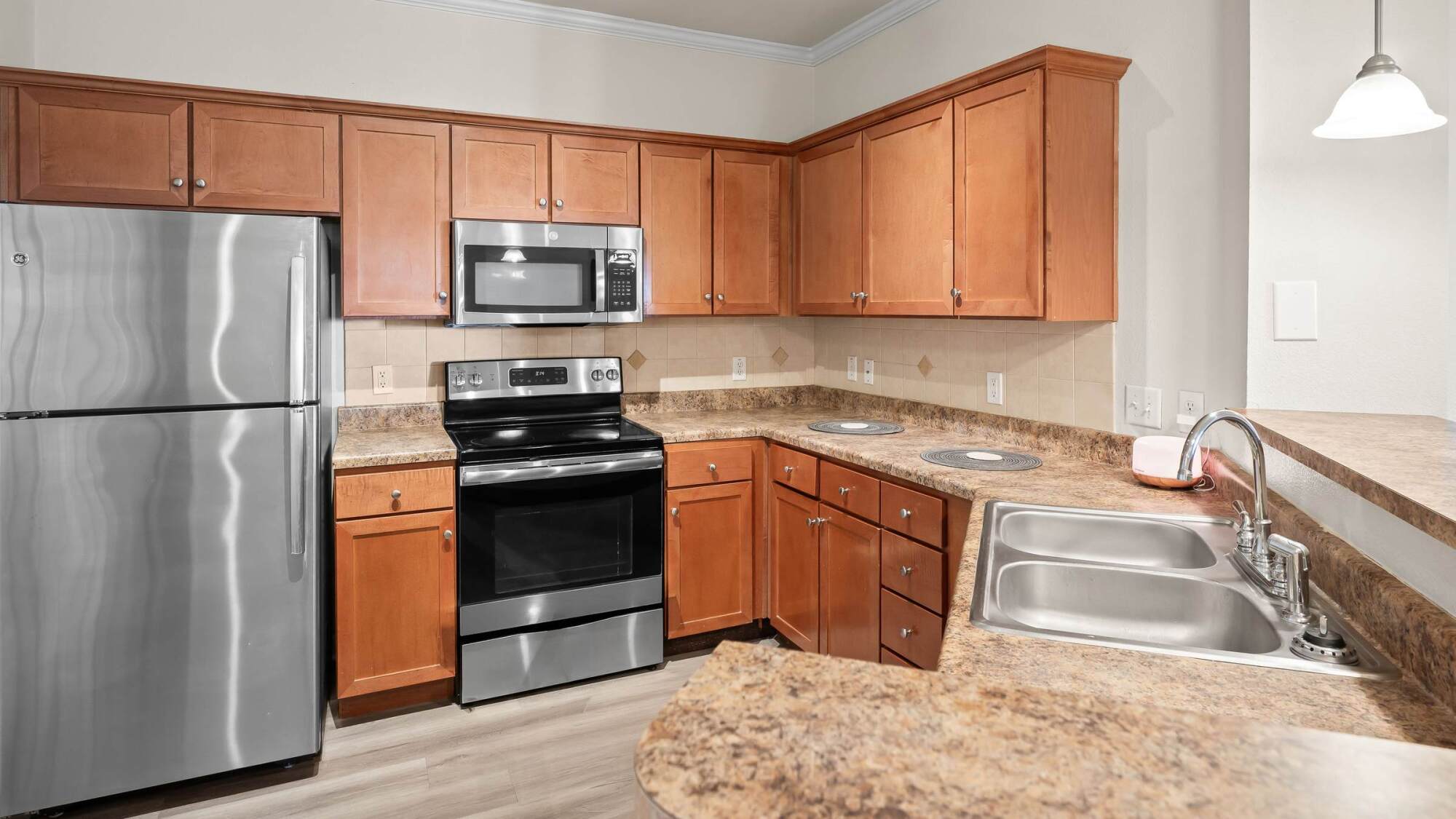 Modern kitchen with wood cabinets, stainless steel appliances, double sink, and marble countertops.
