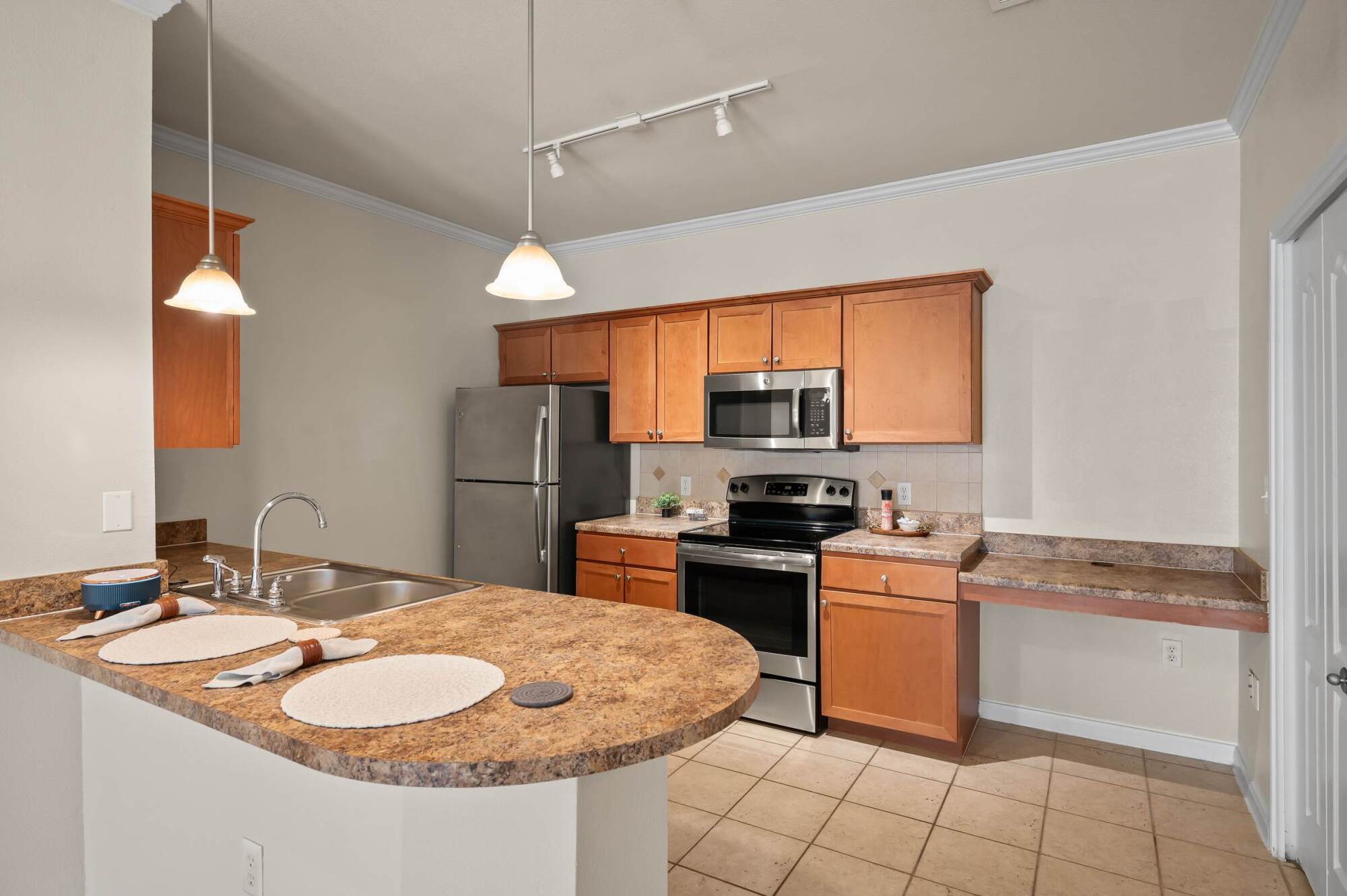 Modern kitchen with brown cabinets, stainless steel appliances, and a curved countertop with place settings.