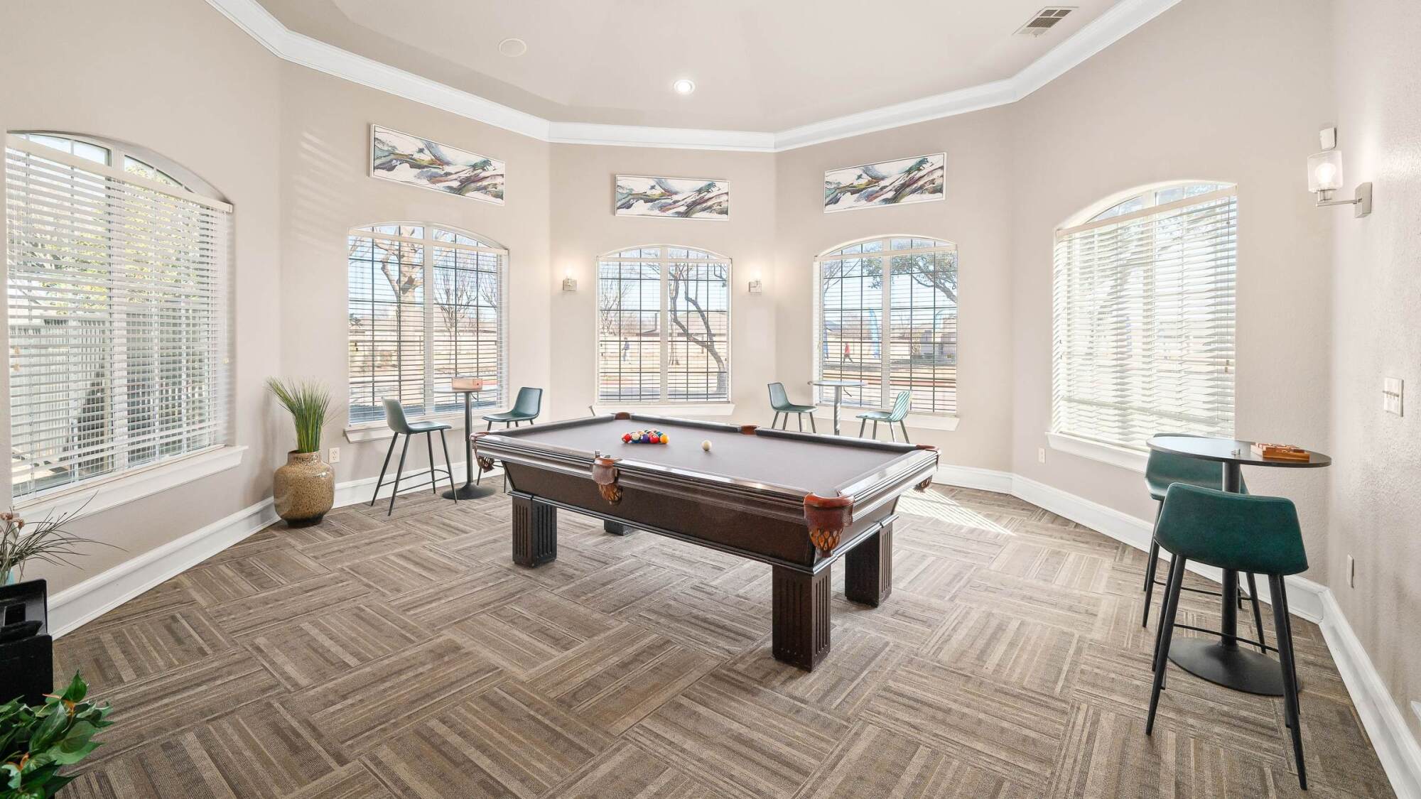 A bright room with a pool table, chairs, round tables, and large windows letting in natural light.
