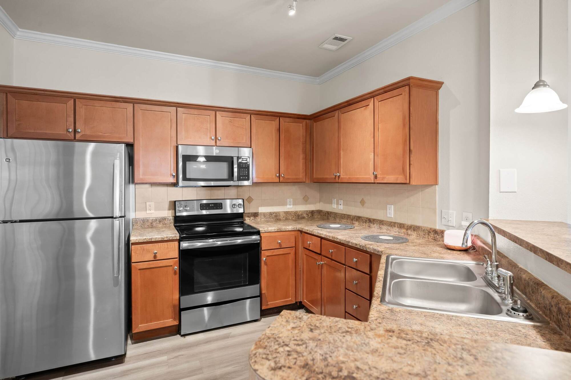 Modern kitchen with wood cabinets, stainless steel appliances, double sink, and marble-look countertops.