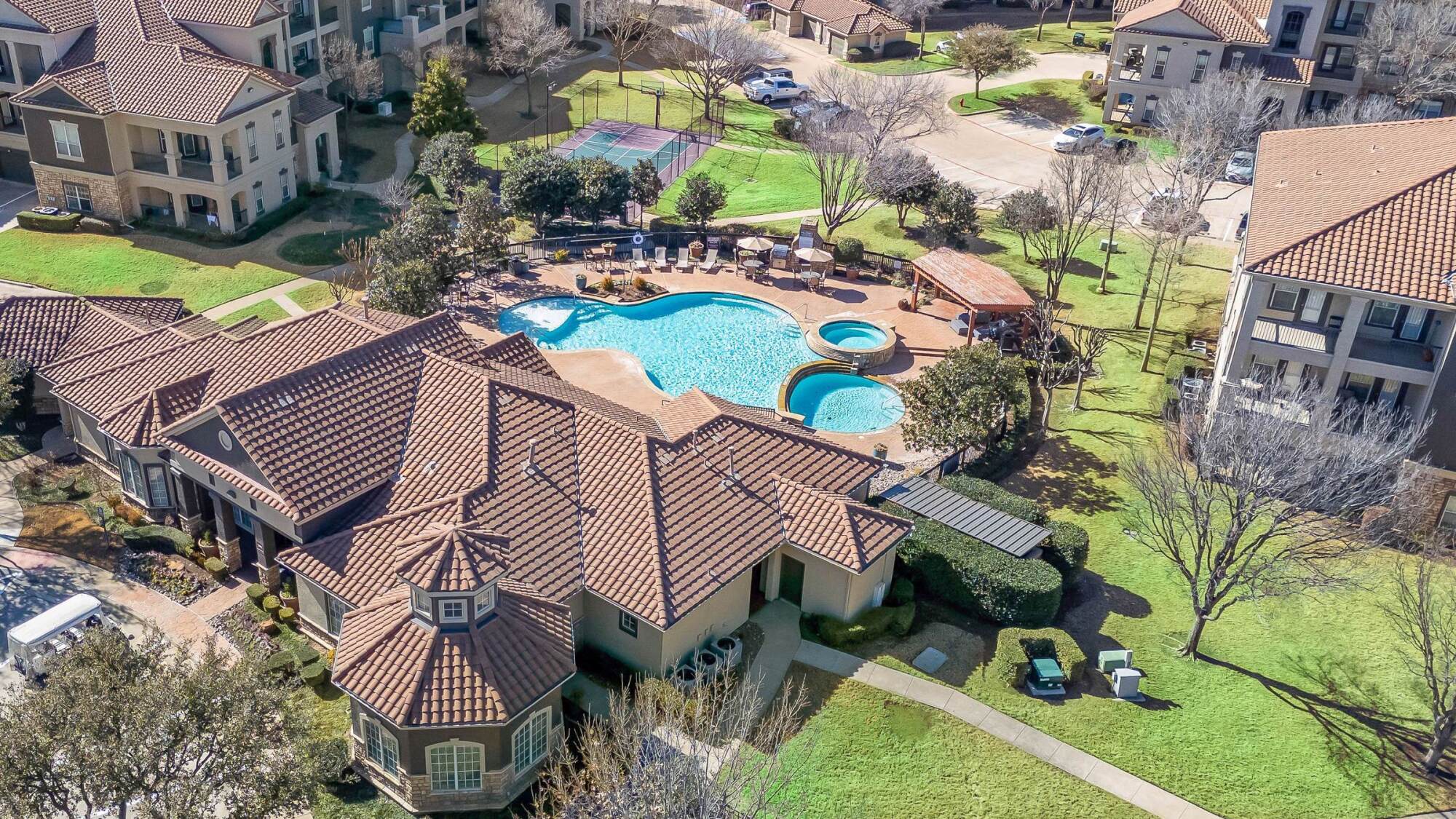 Aerial view of an apartment complex featuring a swimming pool, hot tubs, and landscaped grounds.