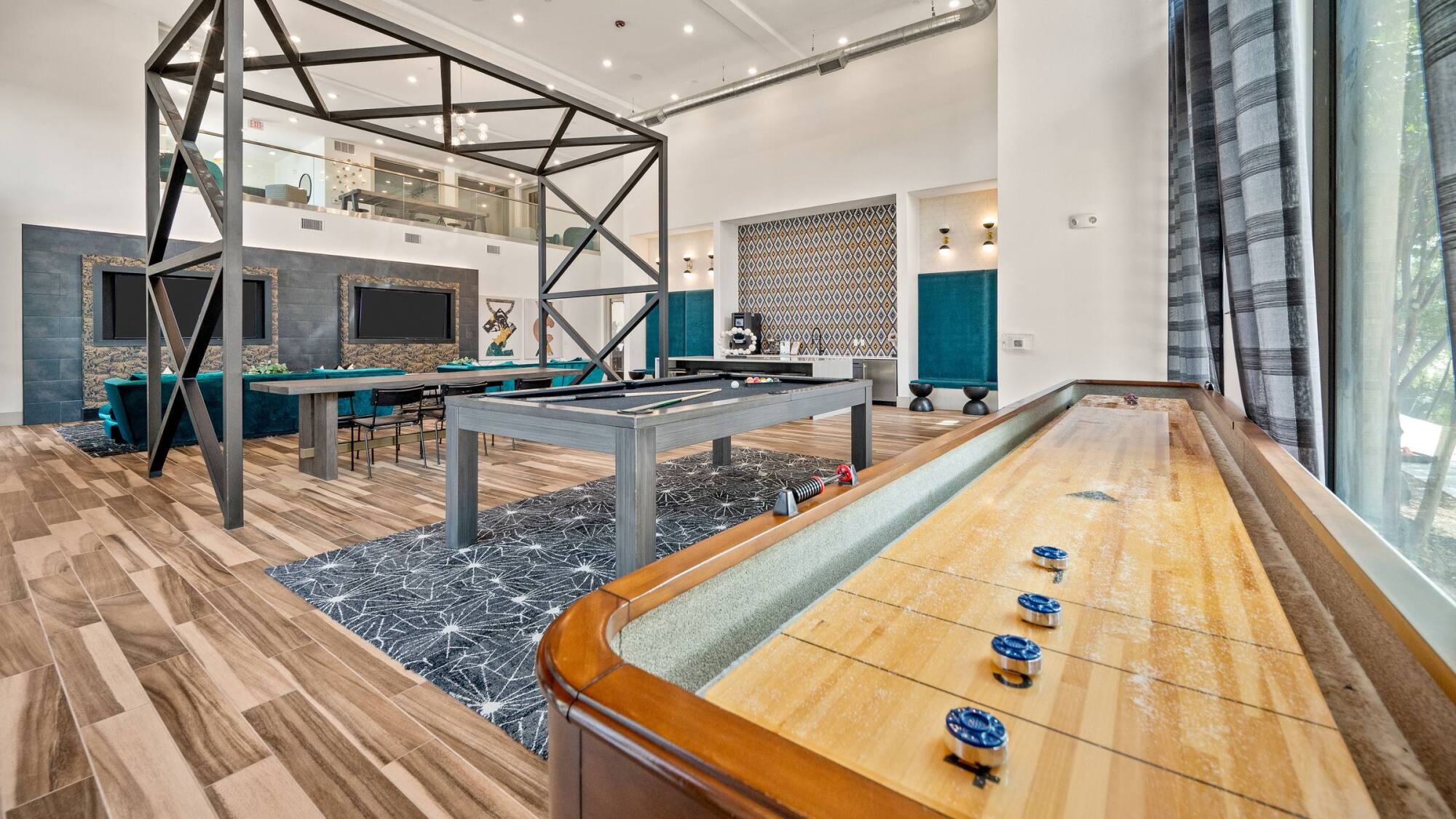 Modern game room with pool table, shuffleboard, and large windows letting in natural light.