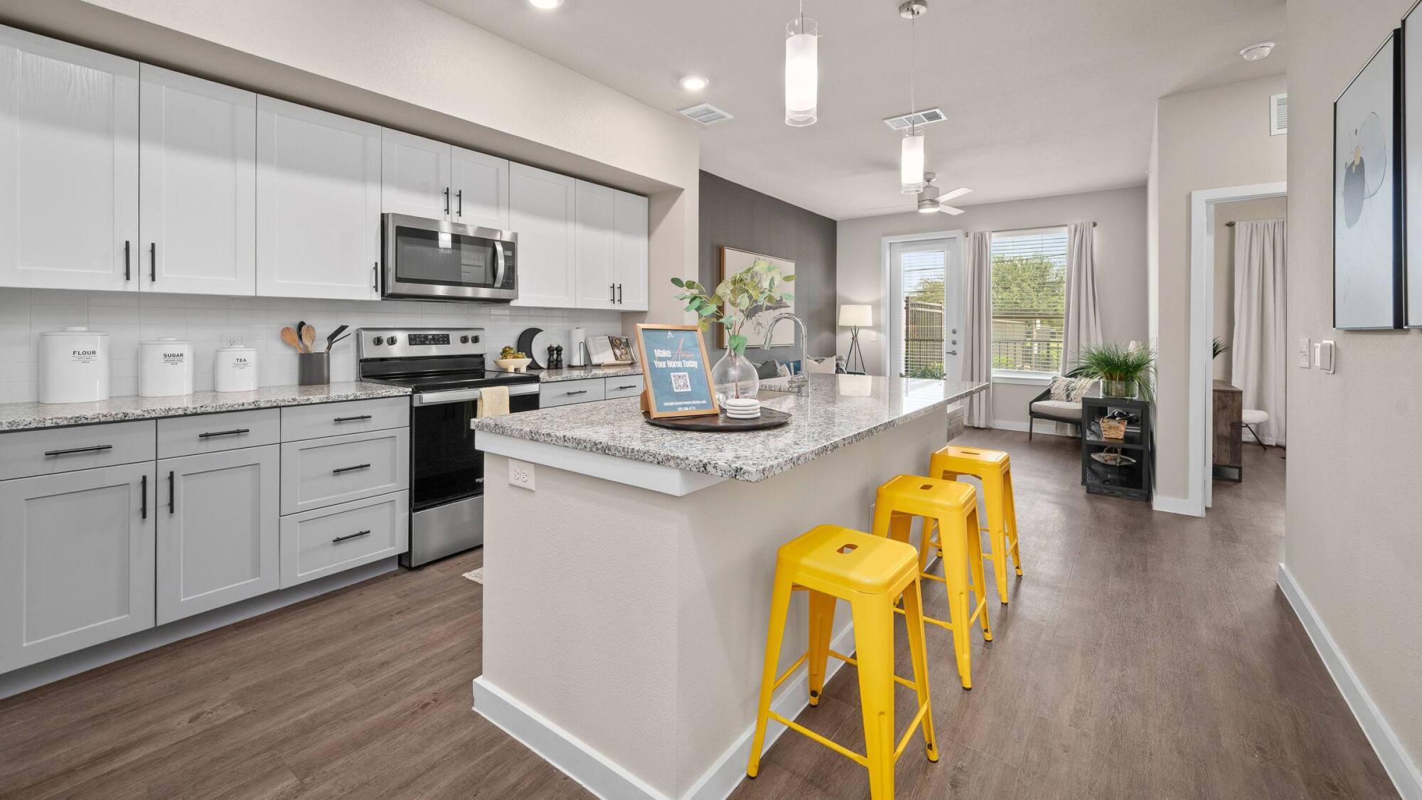 Modern kitchen with white cabinets, stainless steel appliances, and three yellow stools at a granite island.
