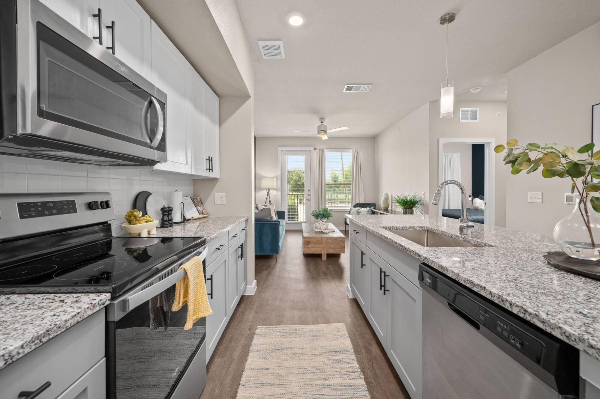 Modern kitchen with granite countertops, stainless steel appliances, and view into a bright living room.